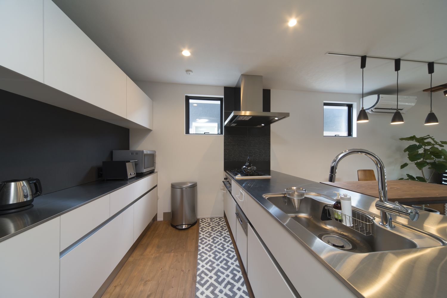 扉付きのカップボードが背面にあるステンレスの天板のペニンシュラキッチン・デザイン住宅