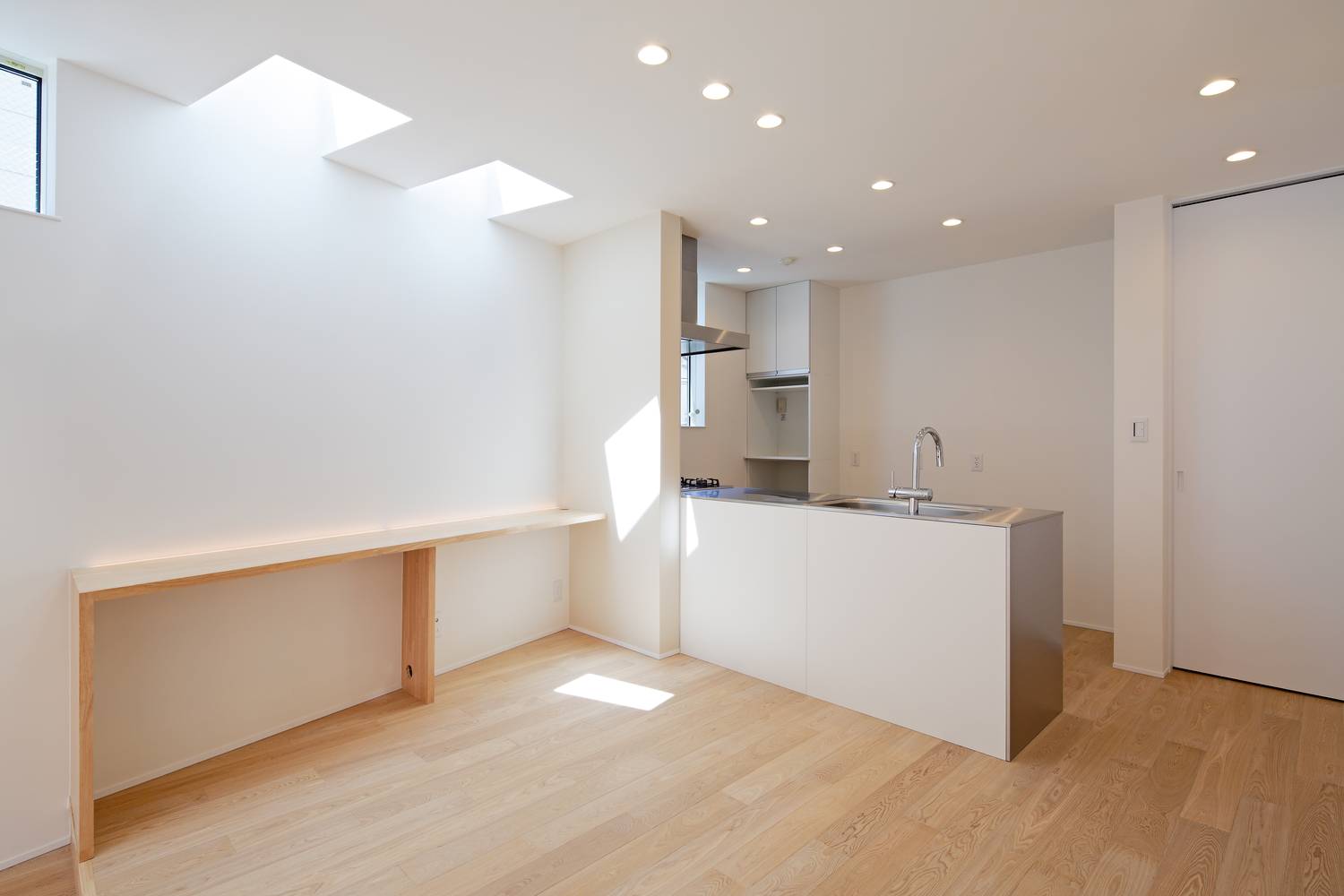 白いカウンターキッチンのそばに、壁付けの木のデスクを置いたトップライトのあるLDK・デザイン住宅 注文住宅・デザイン住宅建築実例_『CASE628 つみ木』_LDK