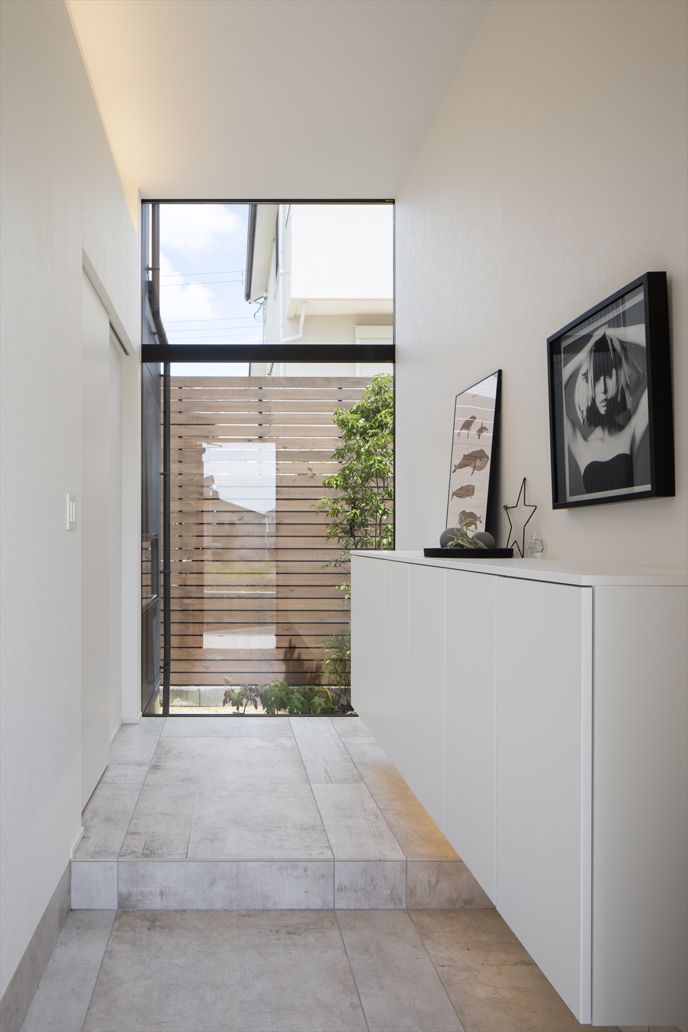 正面に窓がある、白いシューズボックスが壁に付けられたタイルの床の玄関・デザイン住宅 注文住宅・デザイン住宅建築実例_『CASE629 Con』_玄関