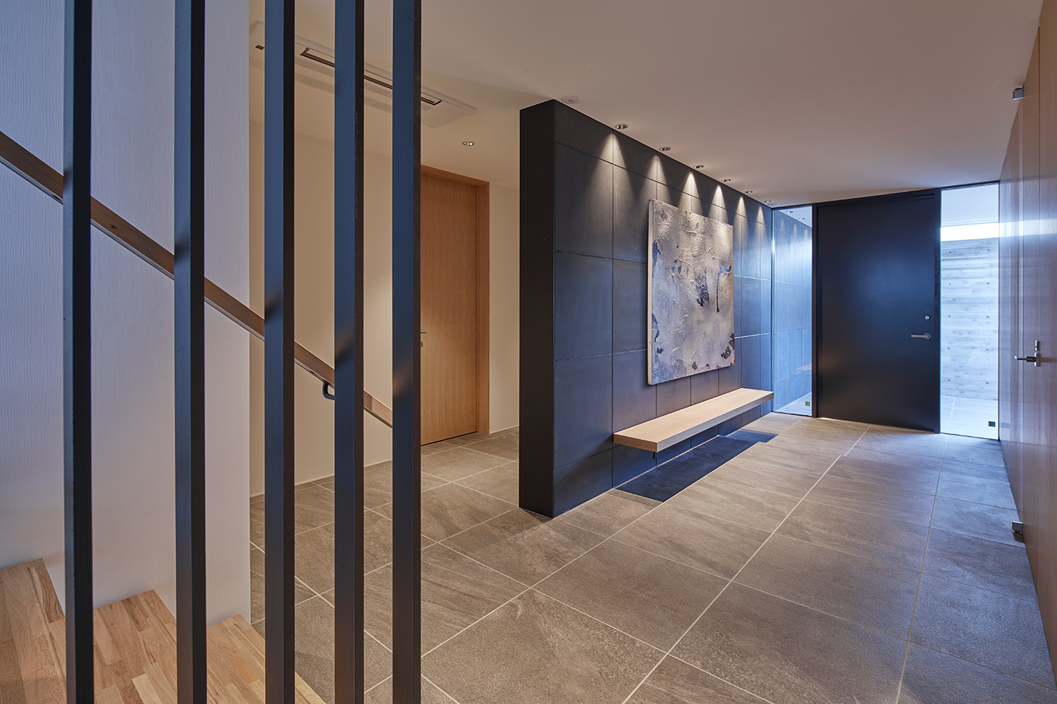 グレーのタイル床で、木製のベンチが取り付けられた黒い壁がある玄関・デザイン住宅 注文住宅・デザイン住宅建築実例_『CASE632 H邸(社長の邸宅)』_玄関