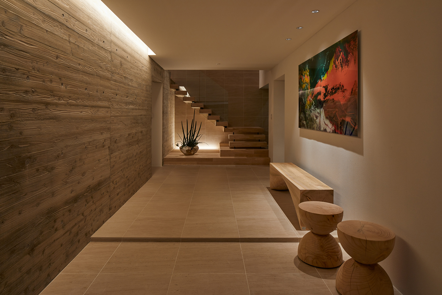 正面に木製の階段があり、木のインテリアや絵画が飾られた空間・デザイン住宅 注文住宅・デザイン住宅建築実例_『CASE678 K邸(社長の邸宅)』_玄関