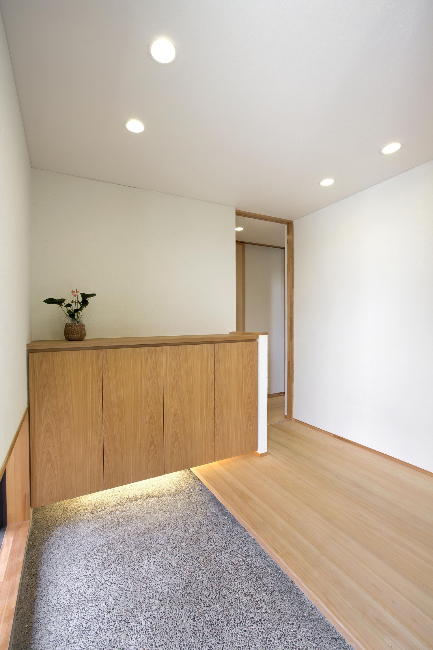 間接照明付きの木のシューズボックスがあるシンプルな玄関・デザイン住宅