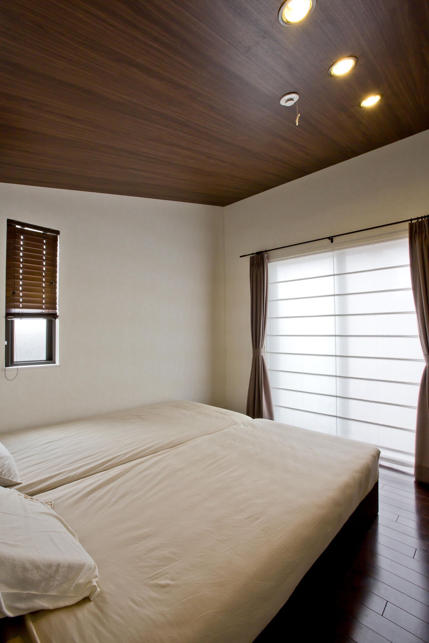 濃い色の木目の天井がある自然光が入る寝室・デザイン住宅