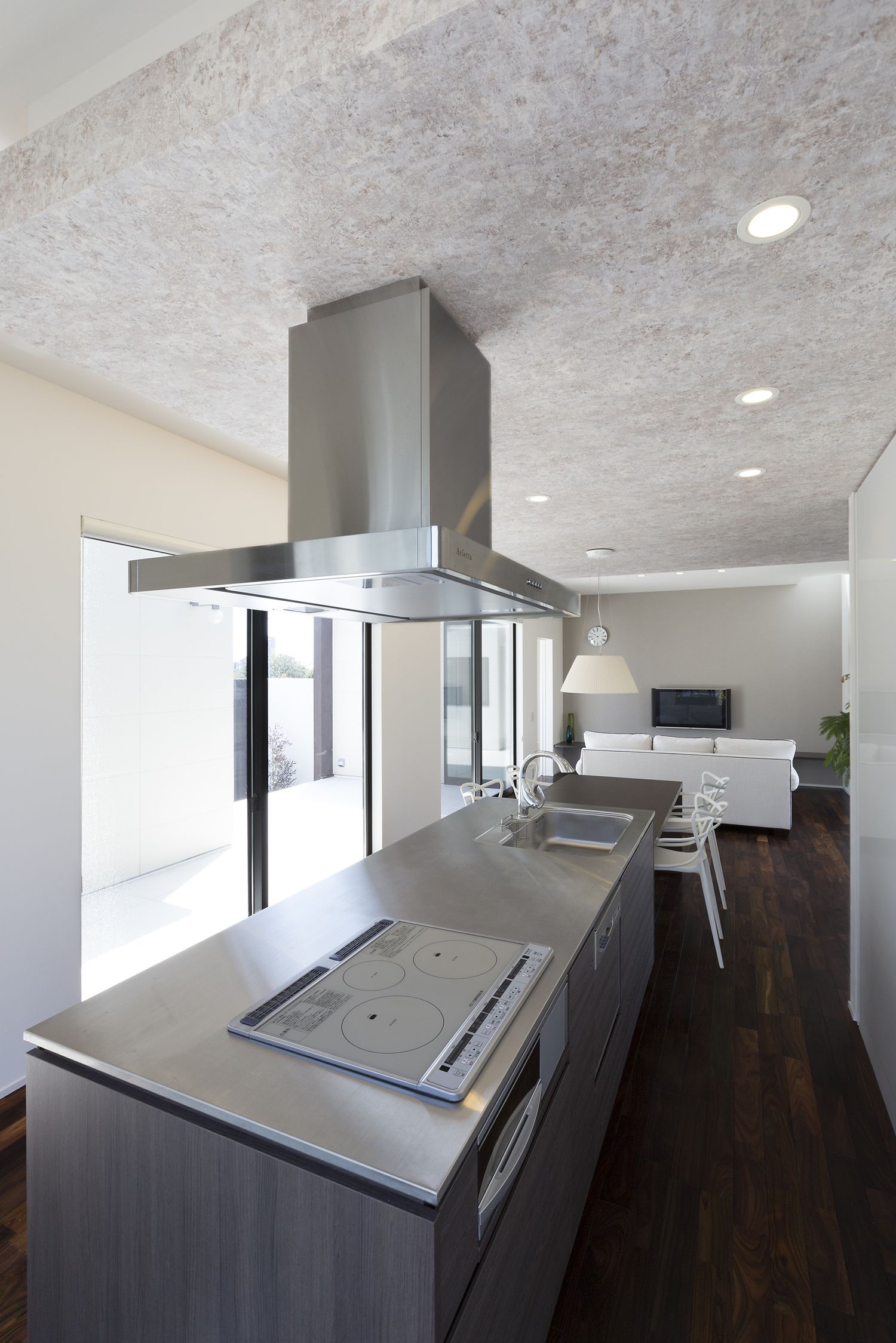 中庭に面した大きな窓の前にステンレスのアイランドキッチンがあるシンプルなLDK・デザイン住宅