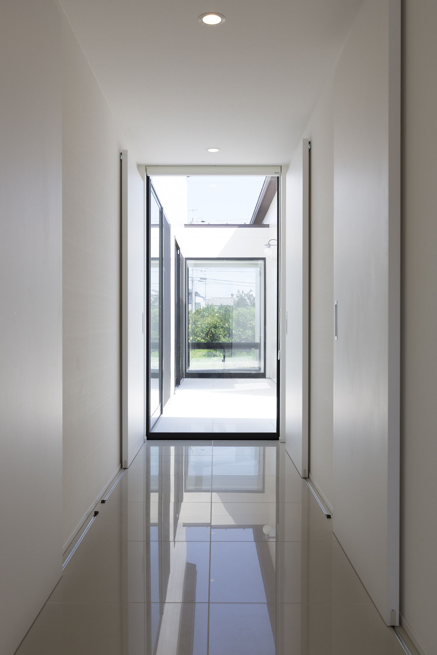 突き当りに窓があるタイル床の開放的な廊下・デザイン住宅