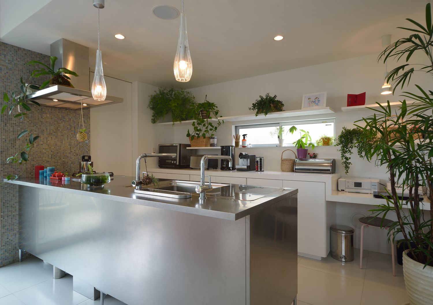 タイルのアクセントや観葉植物があるステンレスのペニンシュラキッチン・デザイン住宅