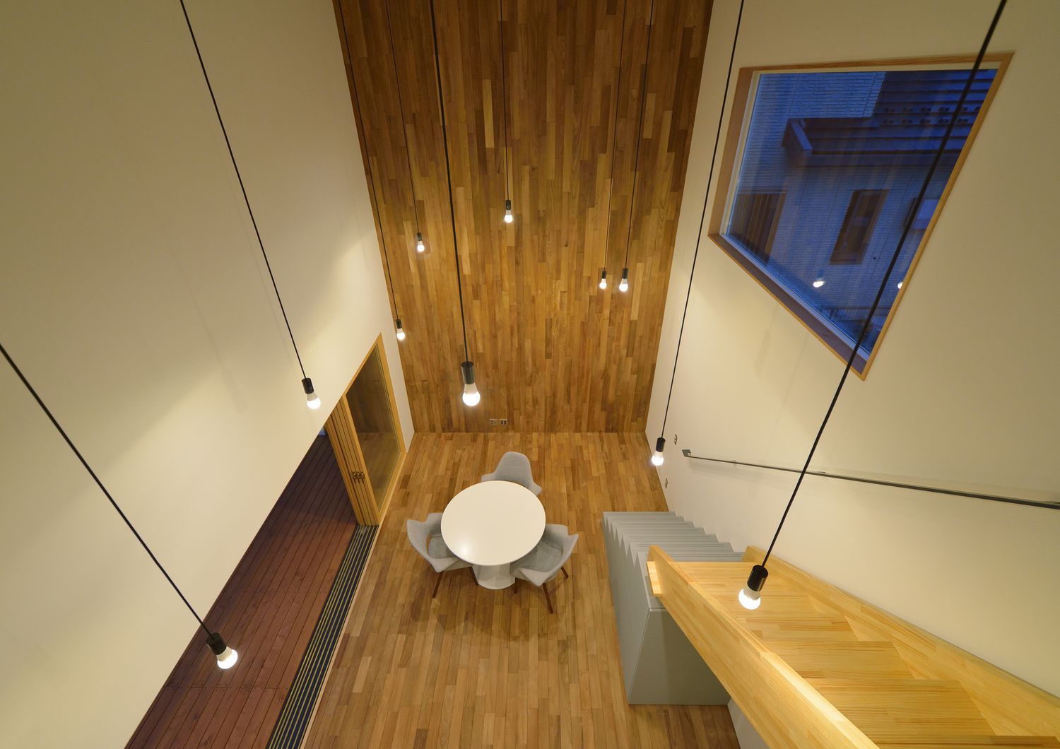 木のアクセントウォールがありシンプルなペンダントライトが沢山取り付けられている吹き抜け・デザイン住宅