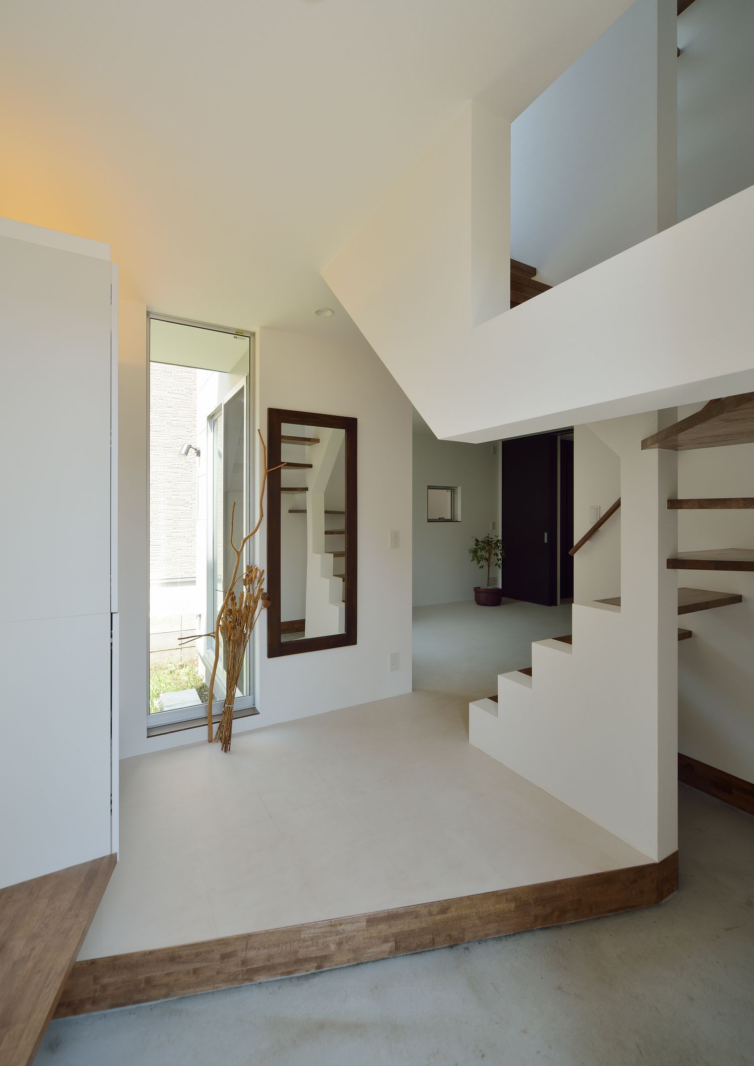 吹き抜けのスケルトン階段の隣にあるモルタルの玄関・デザイン住宅