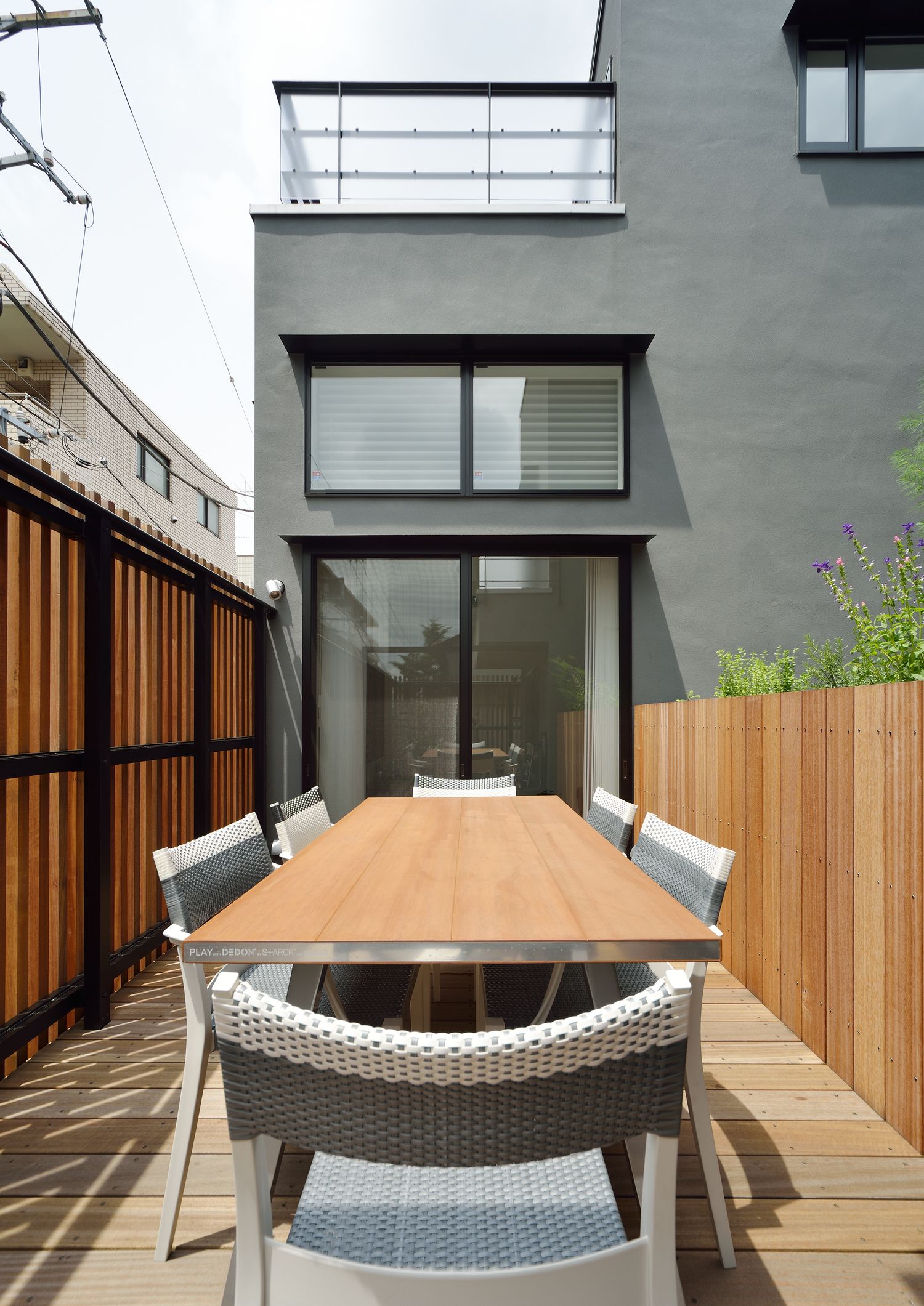 ルーバーの壁に囲まれた椅子とテーブルが置かれたバルコニー・デザイン住宅