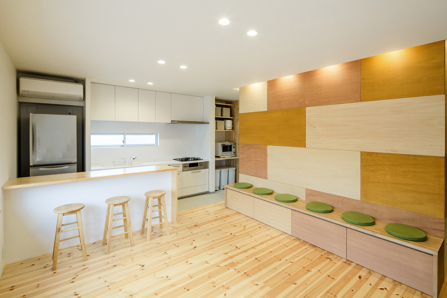 色の違う木材を組み合わせた壁の前にベンチを作り緑色のクッションを置いたLDK・デザイン住宅 注文住宅・デザイン住宅建築実例_『CASE636 cube+』_LDK