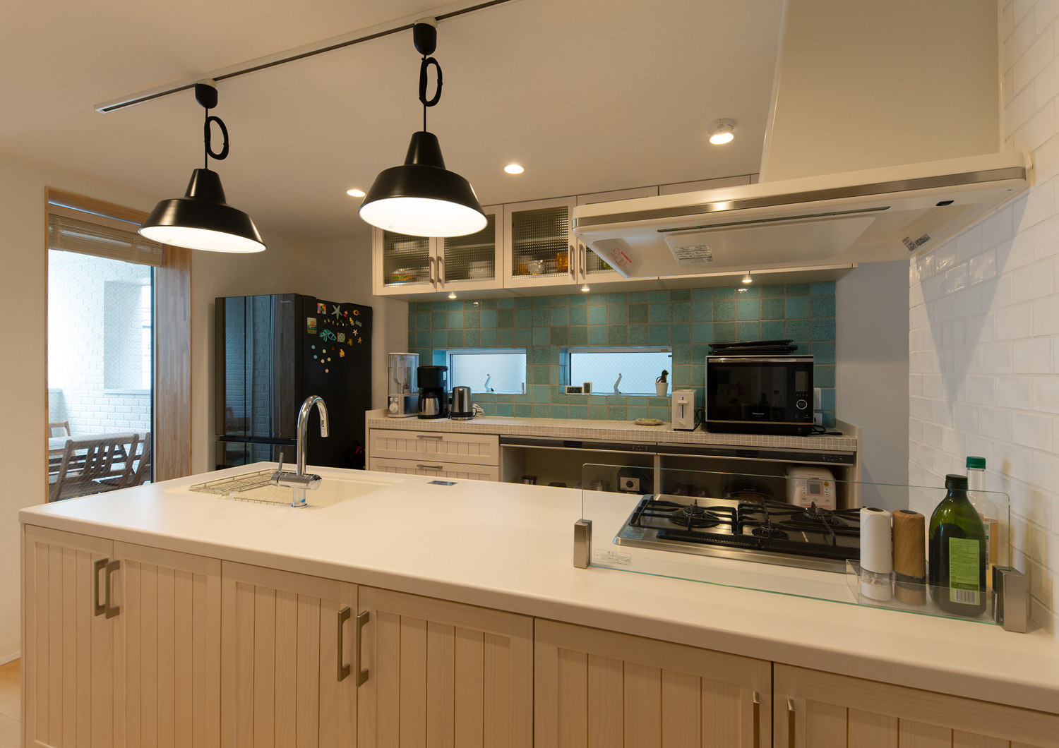 黒いペンダントライトに照らされる、背面の壁に青いタイルが張られた白いペニンシュラキッチン・デザイン住宅 注文住宅・デザイン住宅建築実例_『CASE641 だんだん』_キッチン