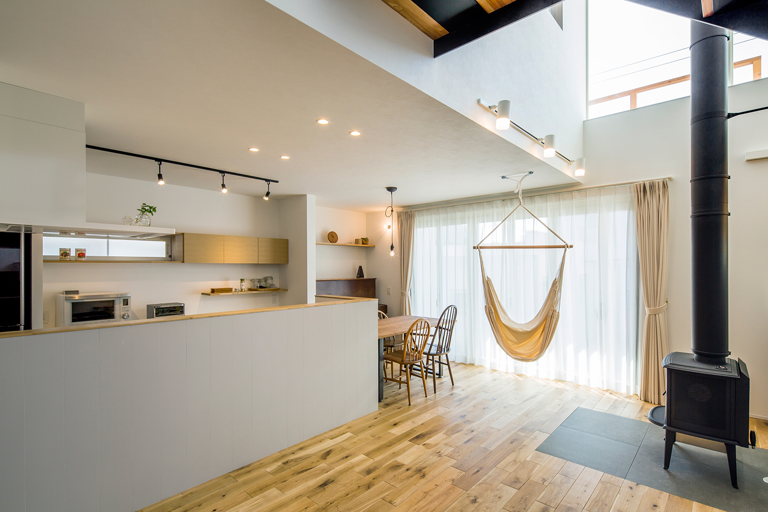 窓際にハンモックがつるされた、腰壁付きのカウンターキッチンがある吹き抜けのLDK・デザイン住宅 注文住宅・デザイン住宅建築実例_『CASE635 三角屋根でつながる家』_LDK