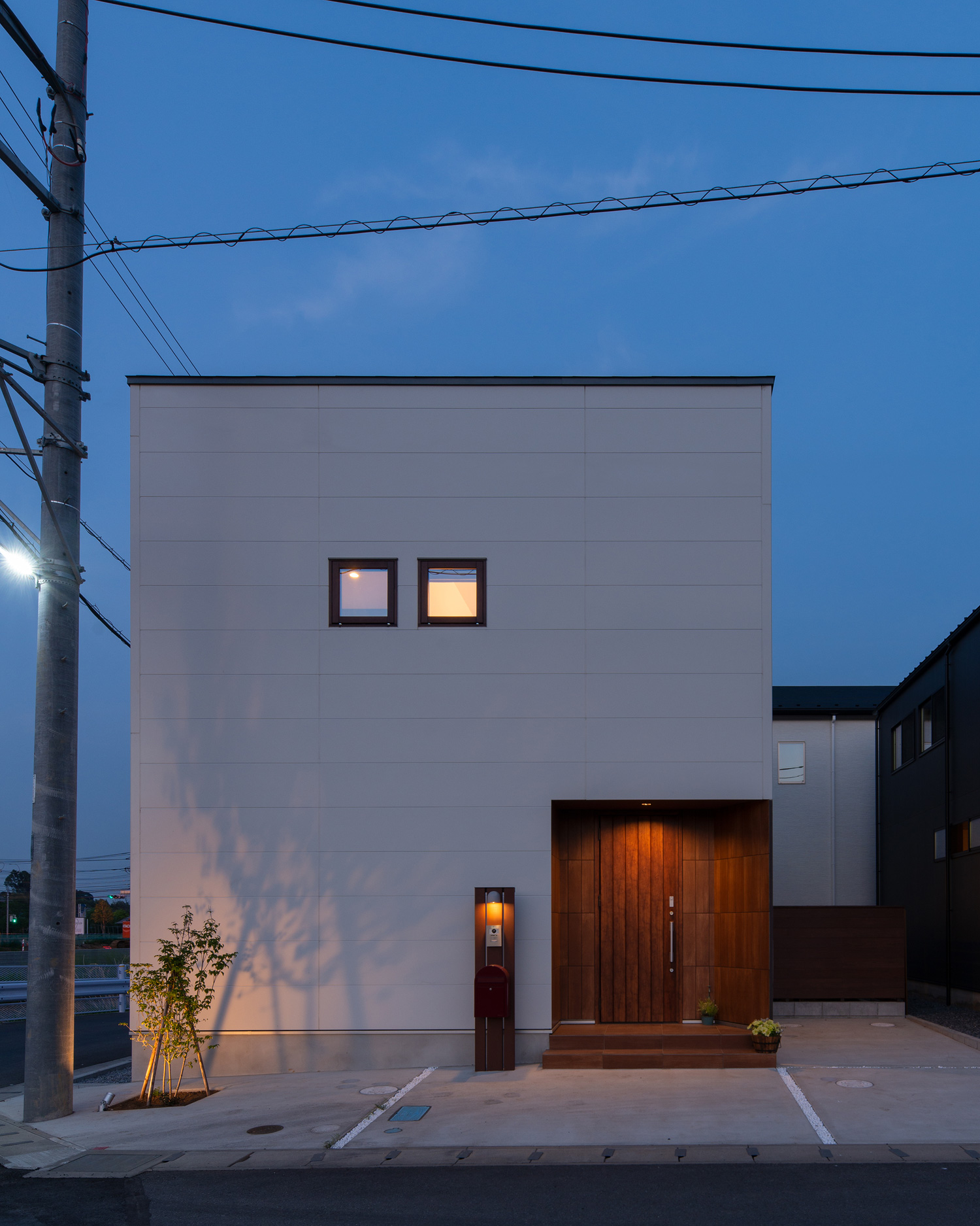 小さな窓が二つ並んだ白いキューブ状の住まいに、植栽が照らされた様子・デザイン住宅 注文住宅・デザイン住宅建築実例_『CASE647 ニコニコハウス』_外観