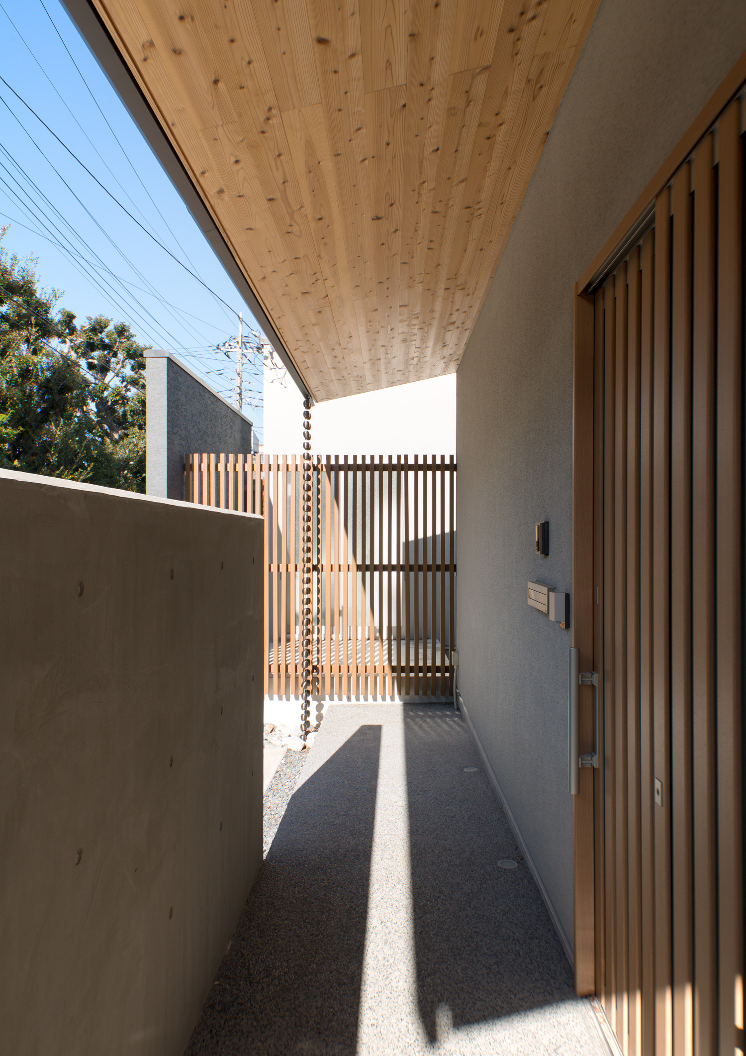木目の庇が取り付けられたアプローチの先にルーバーの目隠しがある様子・デザイン住宅 注文住宅・デザイン住宅建築実例_『CASE649 光の通り道』_外観