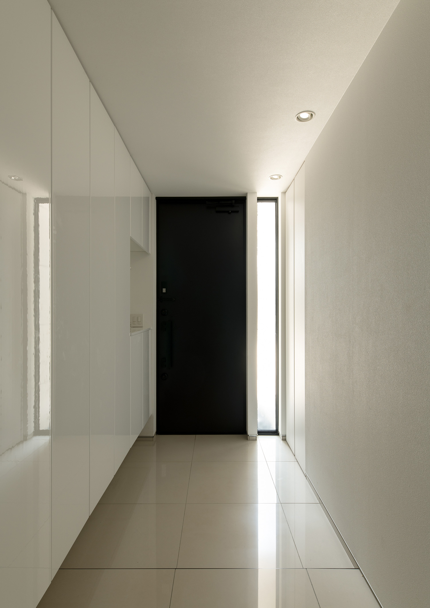 黒い玄関扉の横に縦長のスリット窓が設けられた白いタイルの玄関・デザイン住宅 注文住宅・デザイン住宅建築実例_『CASE653 せんのいえ』_玄関