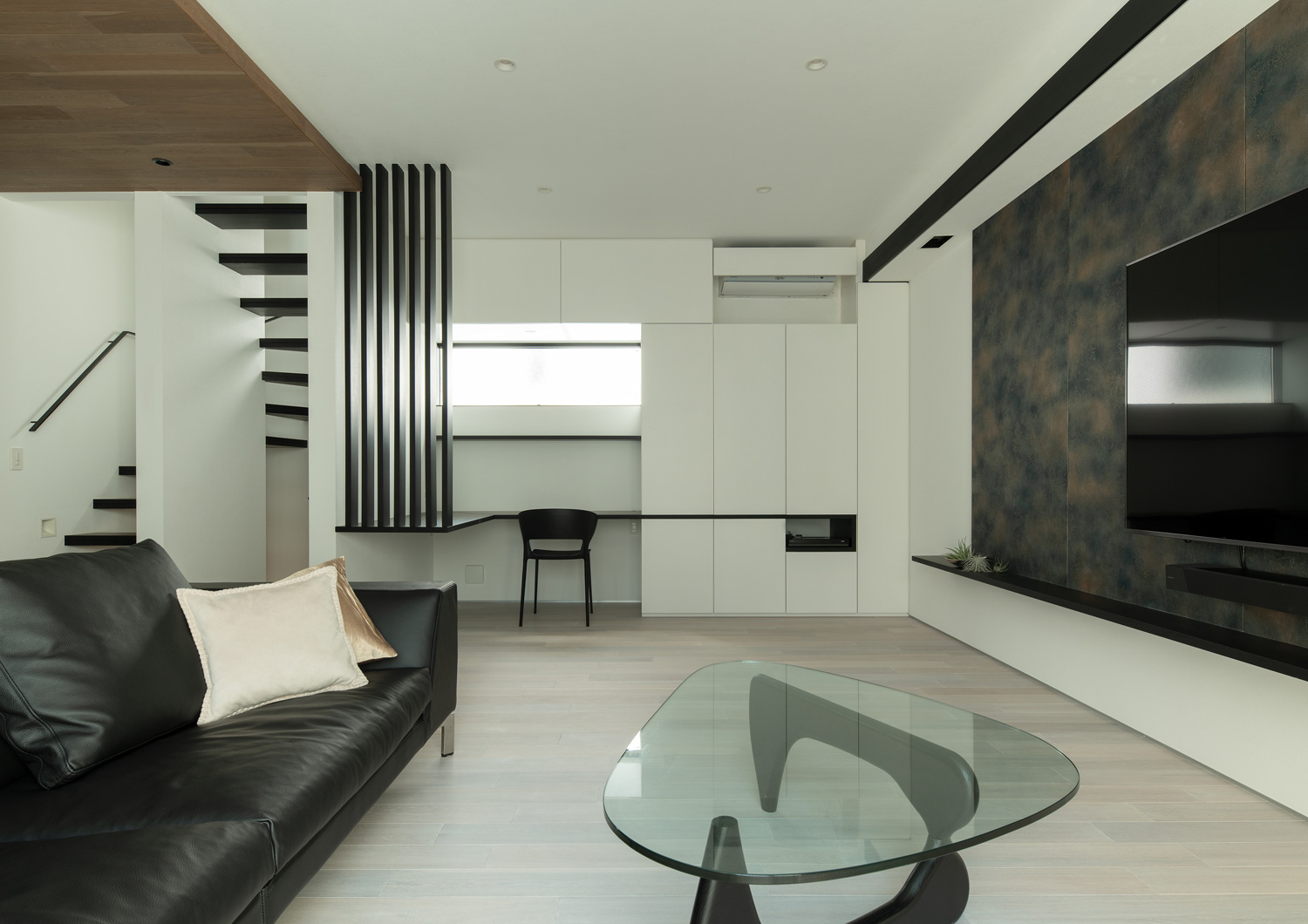 壁付けデスクや壁面収納があり、黒いソファやガラスのサイドテーブルを置いたLDK・デザイン住宅 注文住宅・デザイン住宅建築実例_『CASE653 せんのいえ』_LDK