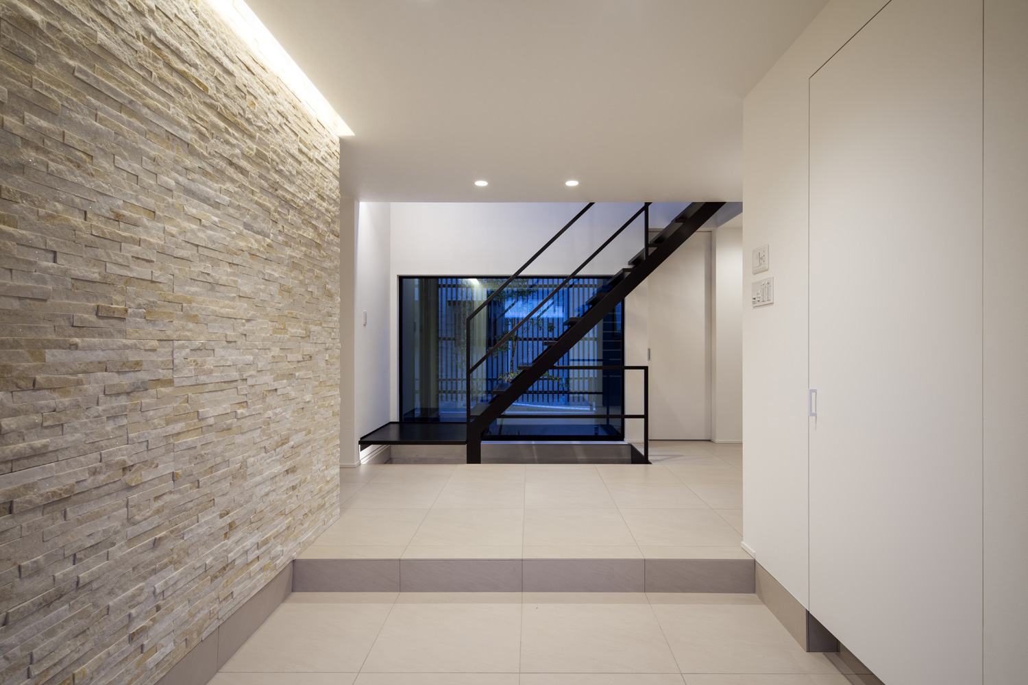 間接照明が取り付けられたタイルの壁がある、明るい玄関・デザイン住宅 注文住宅・デザイン住宅建築実例_『CASE657 La scene』_玄関