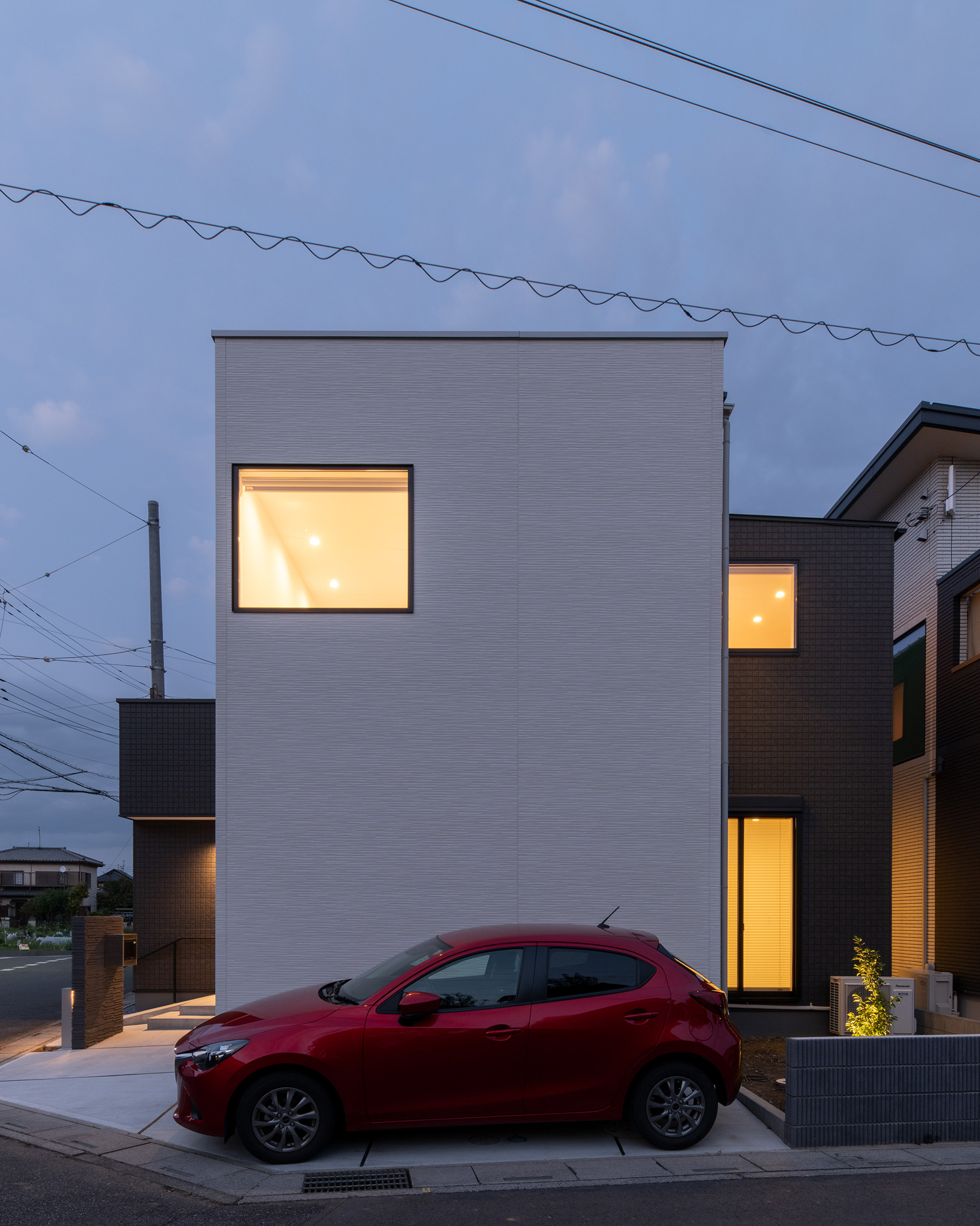 赤い車が止まった白い外壁の住宅の窓から光が漏れる様子・デザイン住宅 注文住宅・デザイン住宅建築実例_『CASE658 connecting terminal』_外観