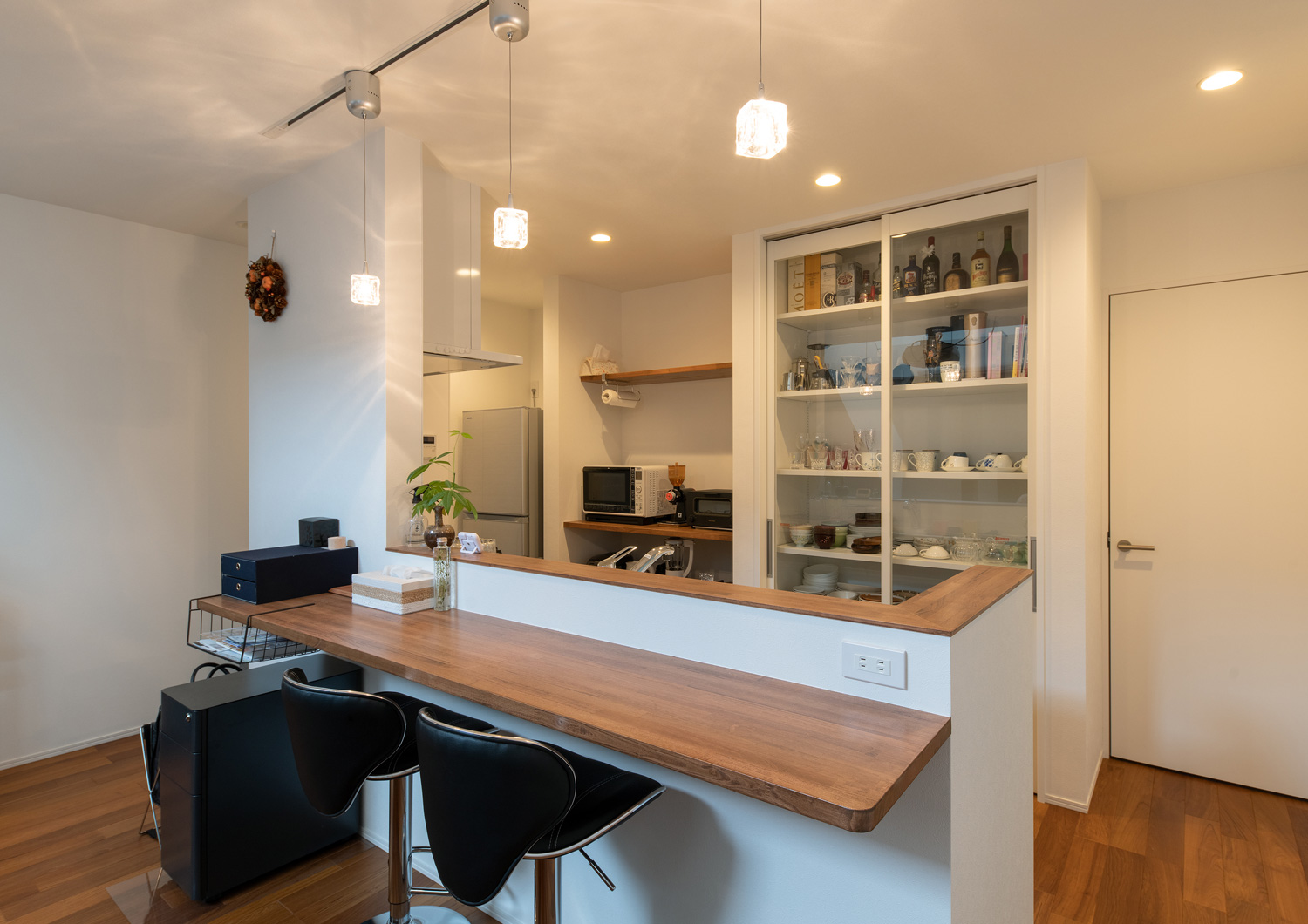 腰壁付きのキッチンに木のカウンターが取り付けられ、ペンダントライトで照らされる様子・デザイン住宅 注文住宅・デザイン住宅建築実例_『CASE658 connecting terminal』_キッチン