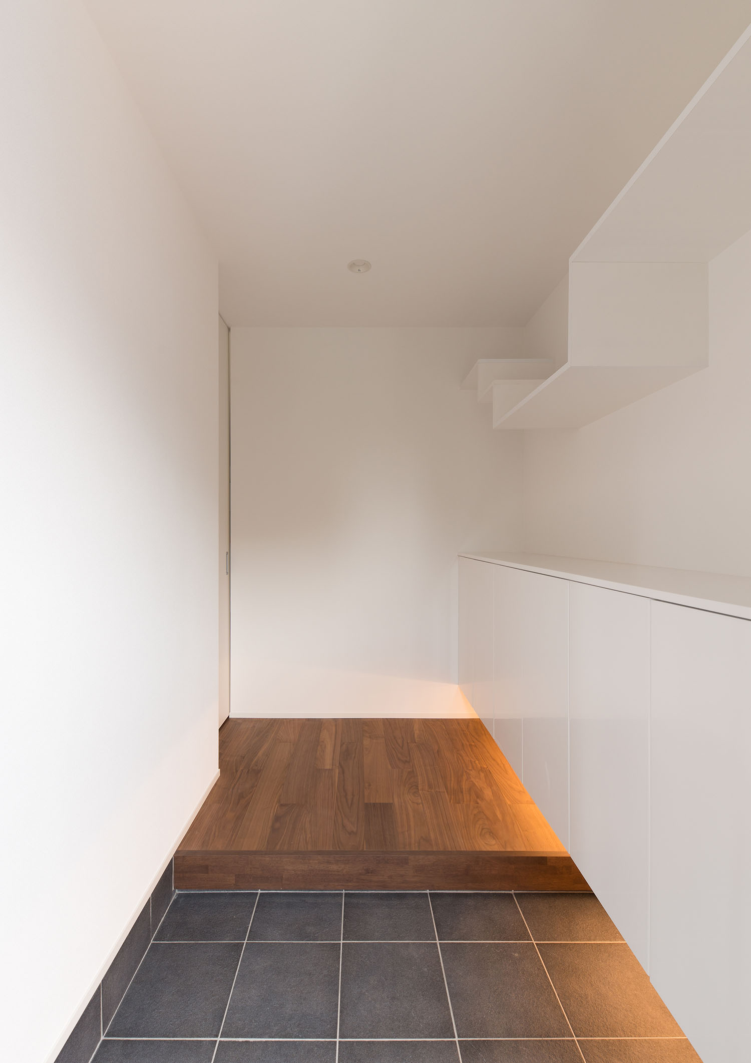 白い壁のタイルの玄関の先に、フローリングの廊下が広がっている様子・デザイン住宅 注文住宅・デザイン住宅建築実例_『CASE662 まくのいえ』_玄関