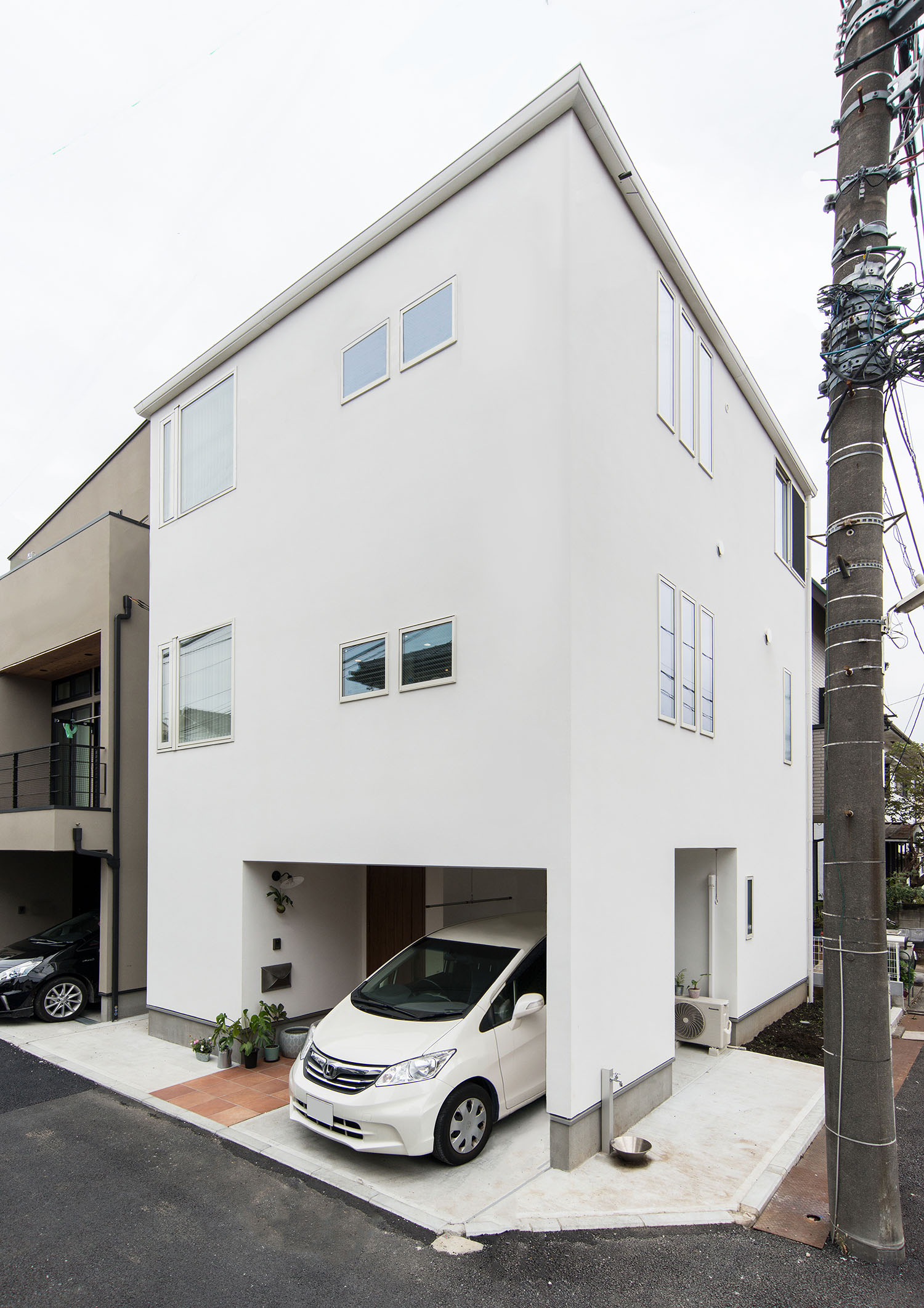 角地に建つ、白いキューブ状の三階建て住宅に白い車が一台止められている様子・デザイン住宅 注文住宅・デザイン住宅建築実例_『CASE674 Gardenのある家』_外観
