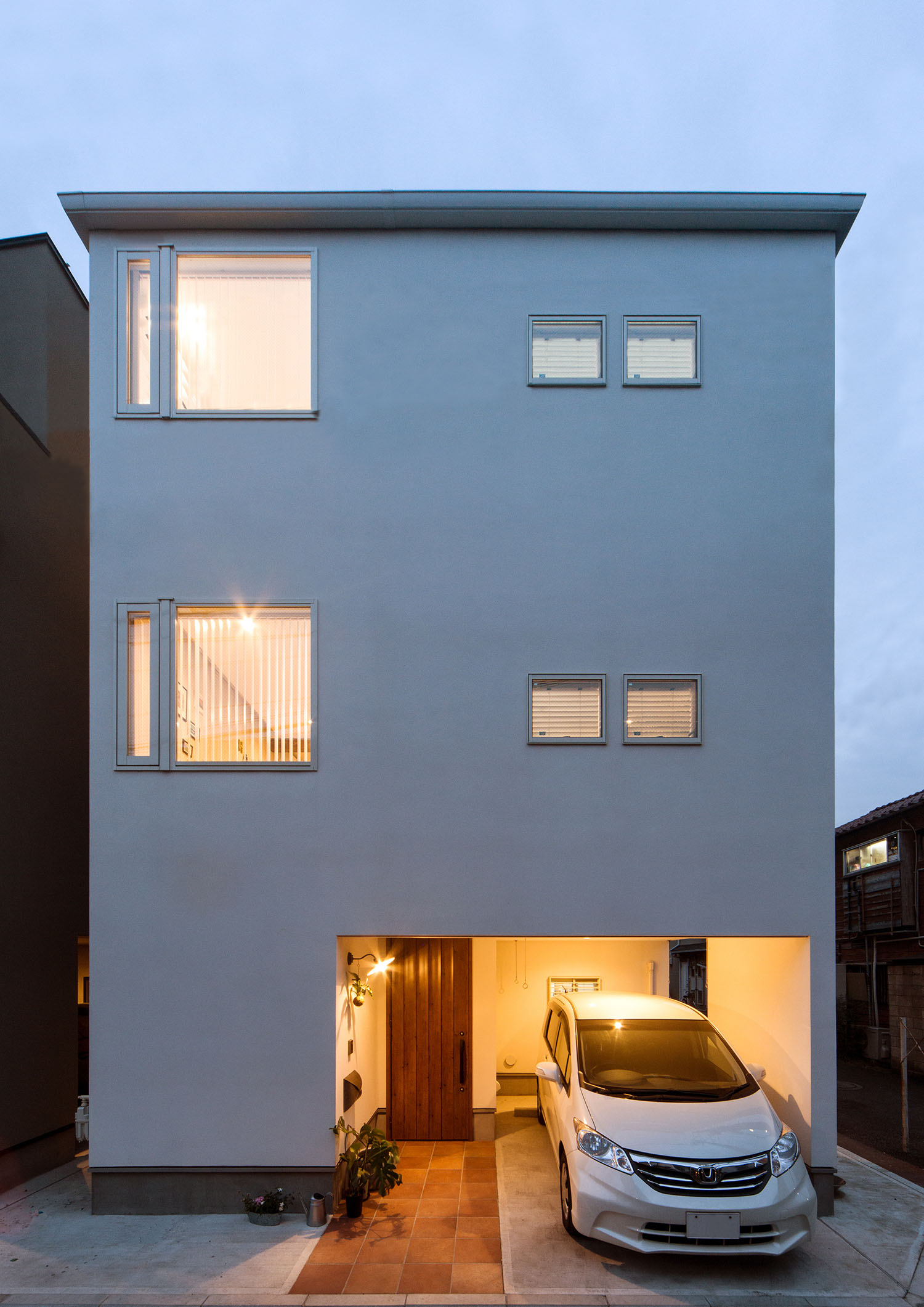 白いキューブ状の三階建て住宅の、窓や玄関から光が漏れている様子・デザイン住宅 注文住宅・デザイン住宅建築実例_『CASE674 Gardenのある家』_外観