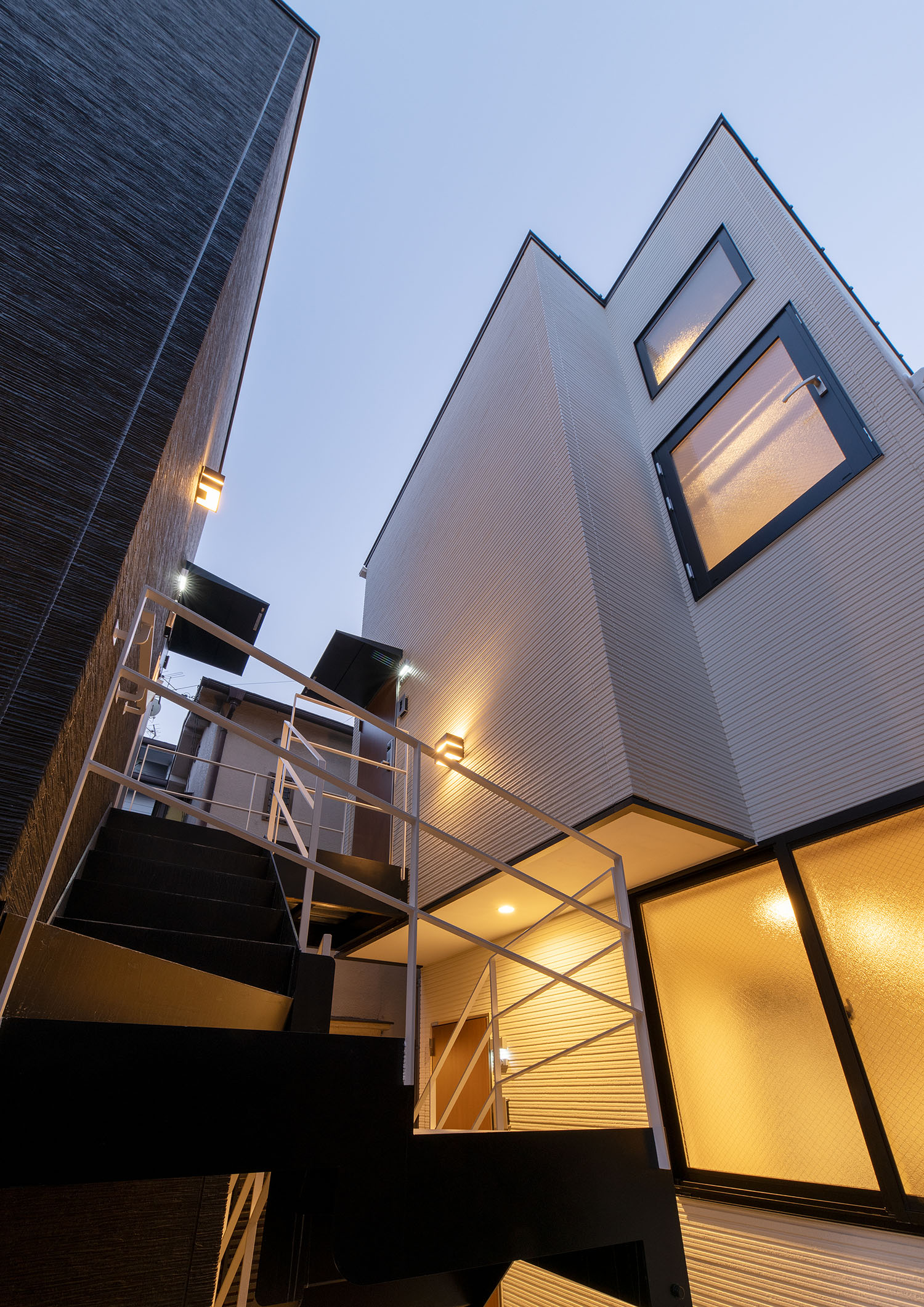 外壁に取り付けられた照明と、窓からの光で照らされる白い外壁の建物・賃貸併用住宅 注文住宅・デザイン住宅建築実例_『CASE681 penche' 「パンシェ」の家』_外観