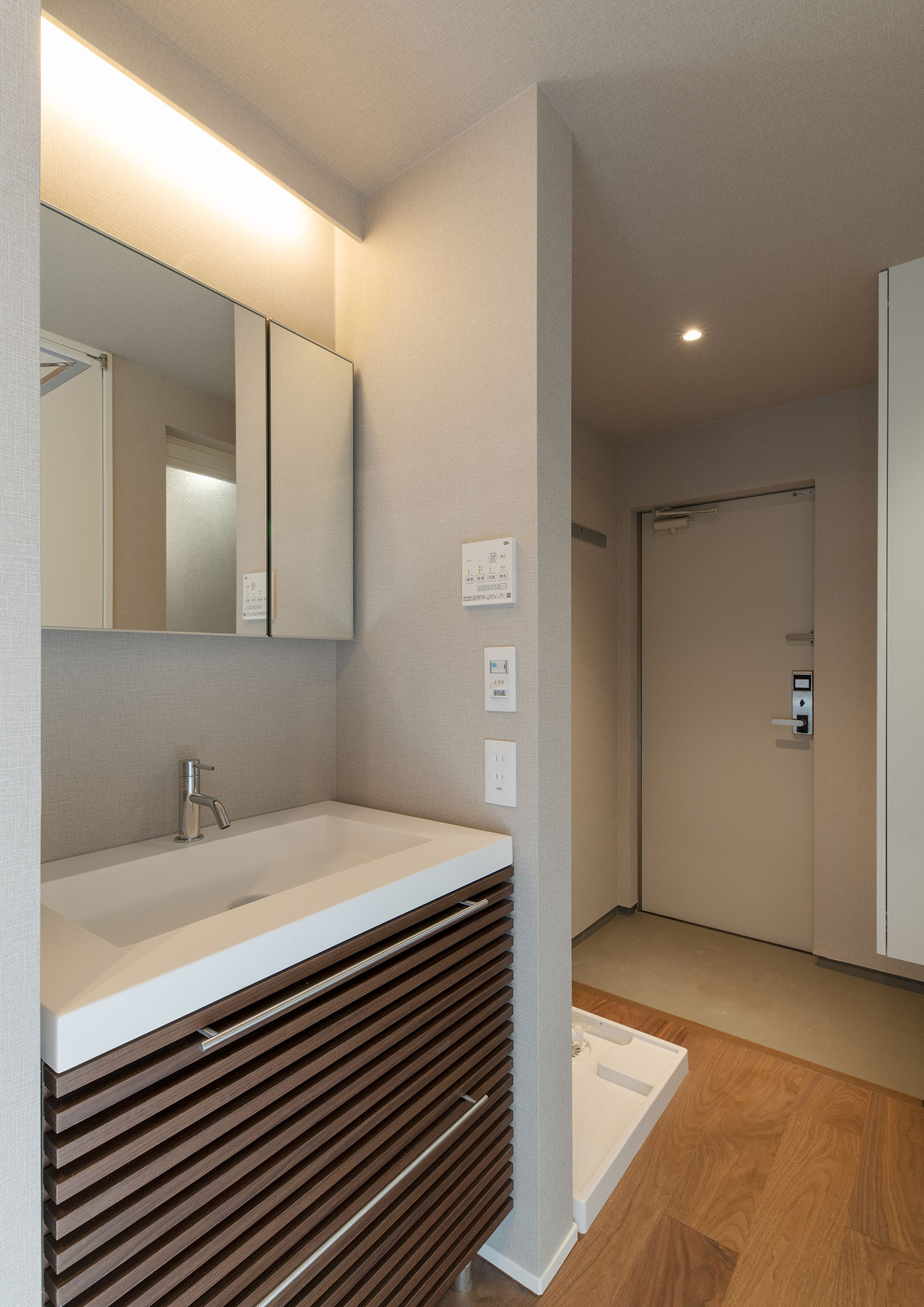 木の引き出しや間接照明が設けられた洗面所越しに玄関が見える様子・賃貸併用住宅 注文住宅・デザイン住宅建築実例_『CASE681 penche' 「パンシェ」の家』_浴室・洗面所