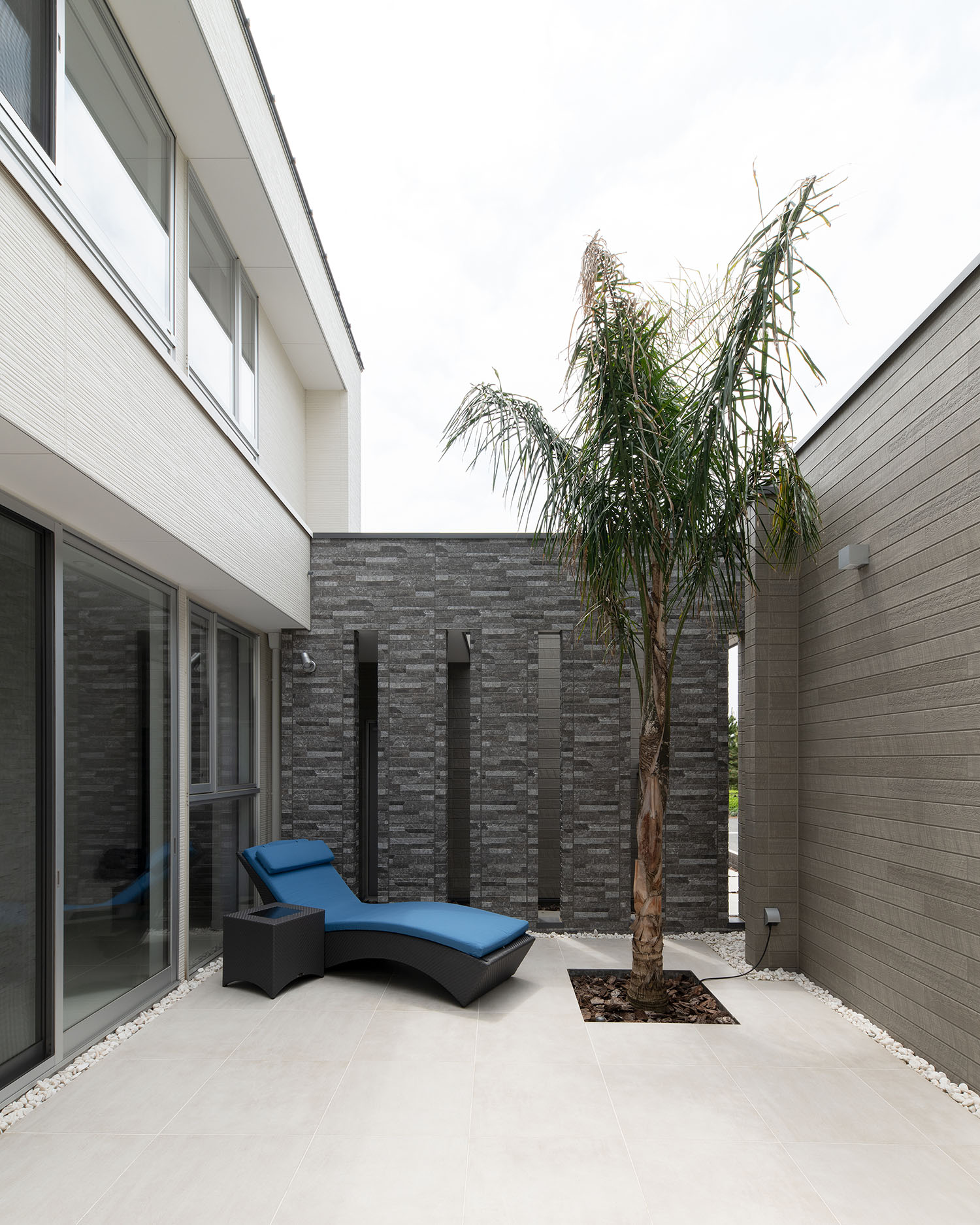 グレーの壁で囲まれておりヤシの木やサンベッドが置かれている中庭・デザイン住宅 注文住宅・デザイン住宅建築実例_『CASE682 Casa de Resort』_中庭