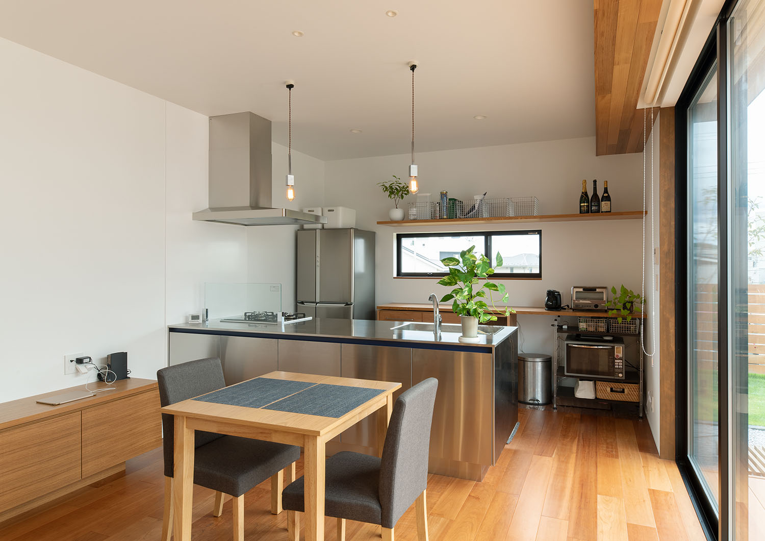 ステンレスのペニンシュラキッチンの前に、二人掛けのダイニングテーブルが置かれている様子・デザイン住宅 注文住宅・デザイン住宅建築実例_『CASE683 丘の上のハウス』_LDK