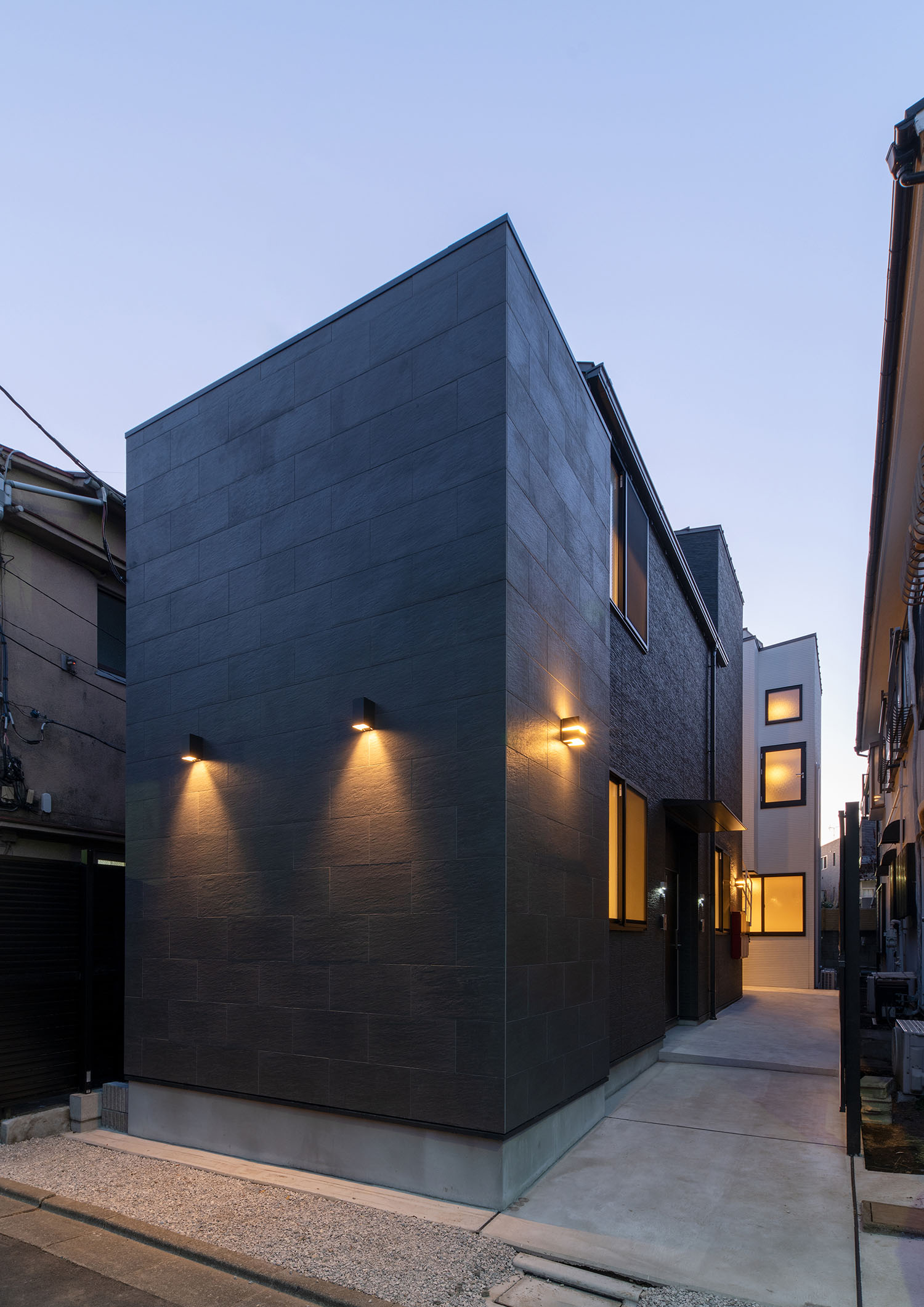 外壁に取り付けられた照明が黒い外壁の建物を照らす様子・賃貸併用住宅 注文住宅・デザイン住宅建築実例_『CASE681 penche' 「パンシェ」の家』_外観