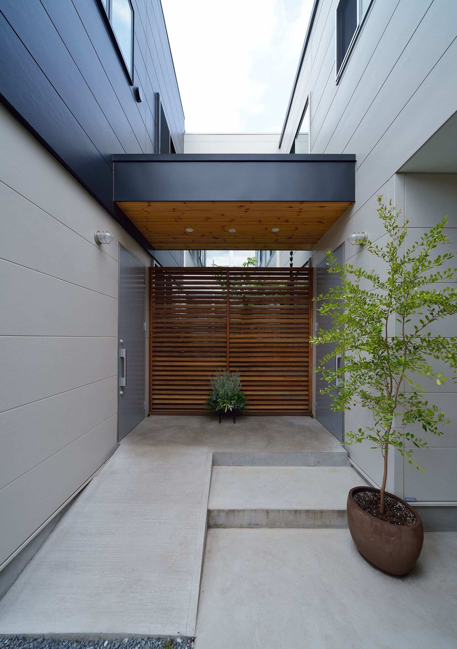 木目の軒天井や木のルーバーがあるコンクリートの玄関ポーチ・デザイン住宅