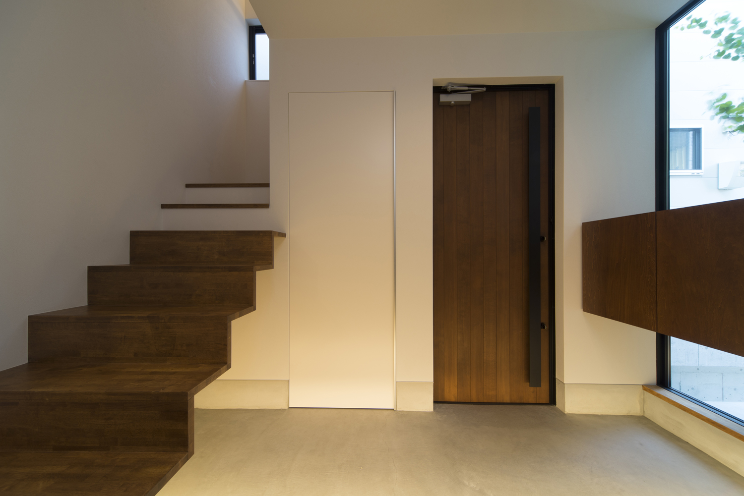 木の玄関扉が取り付けられた大きな窓のあるシンプルな玄関・デザイン住宅