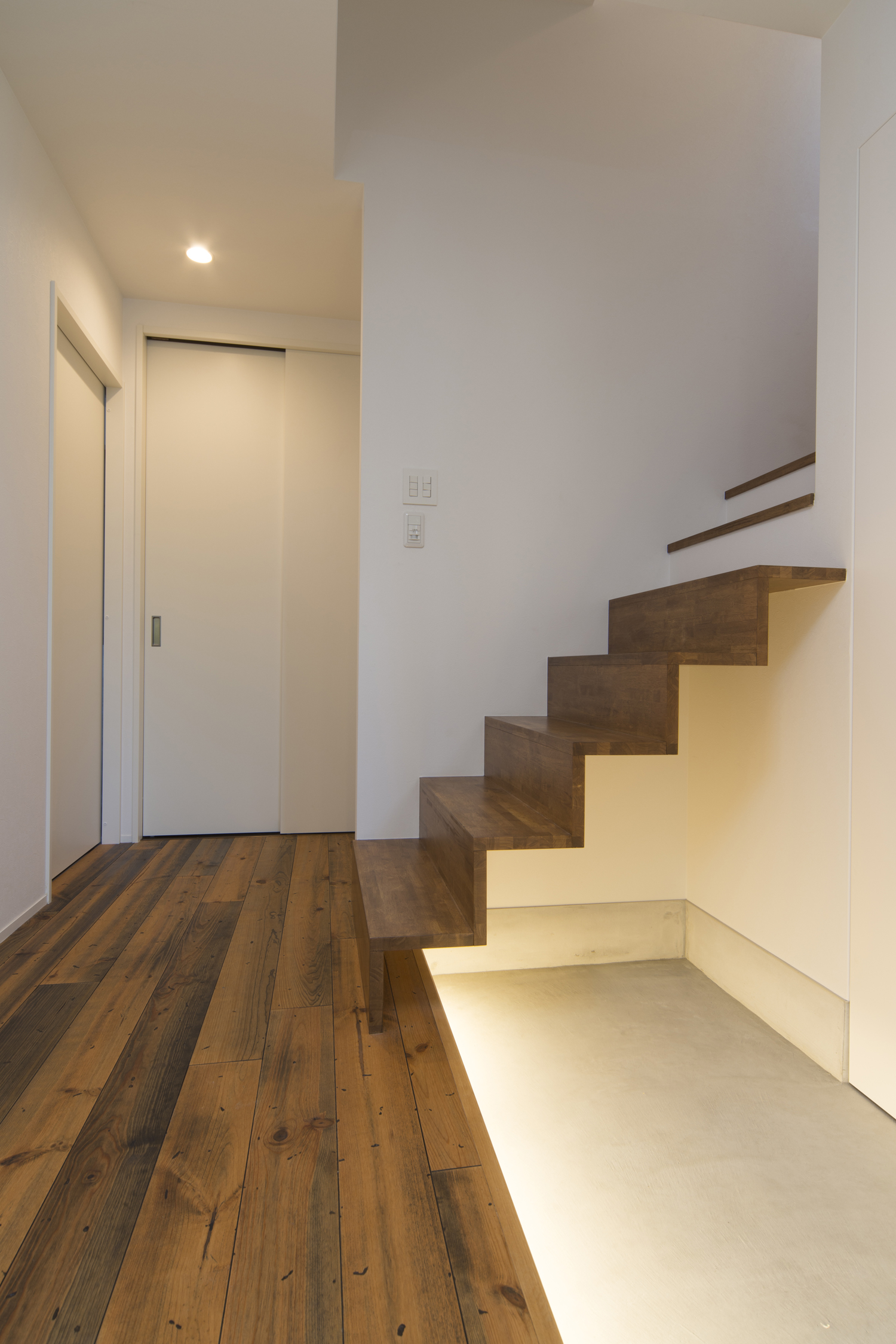 モルタルの玄関を横切る木のスケルトン階段・デザイン住宅