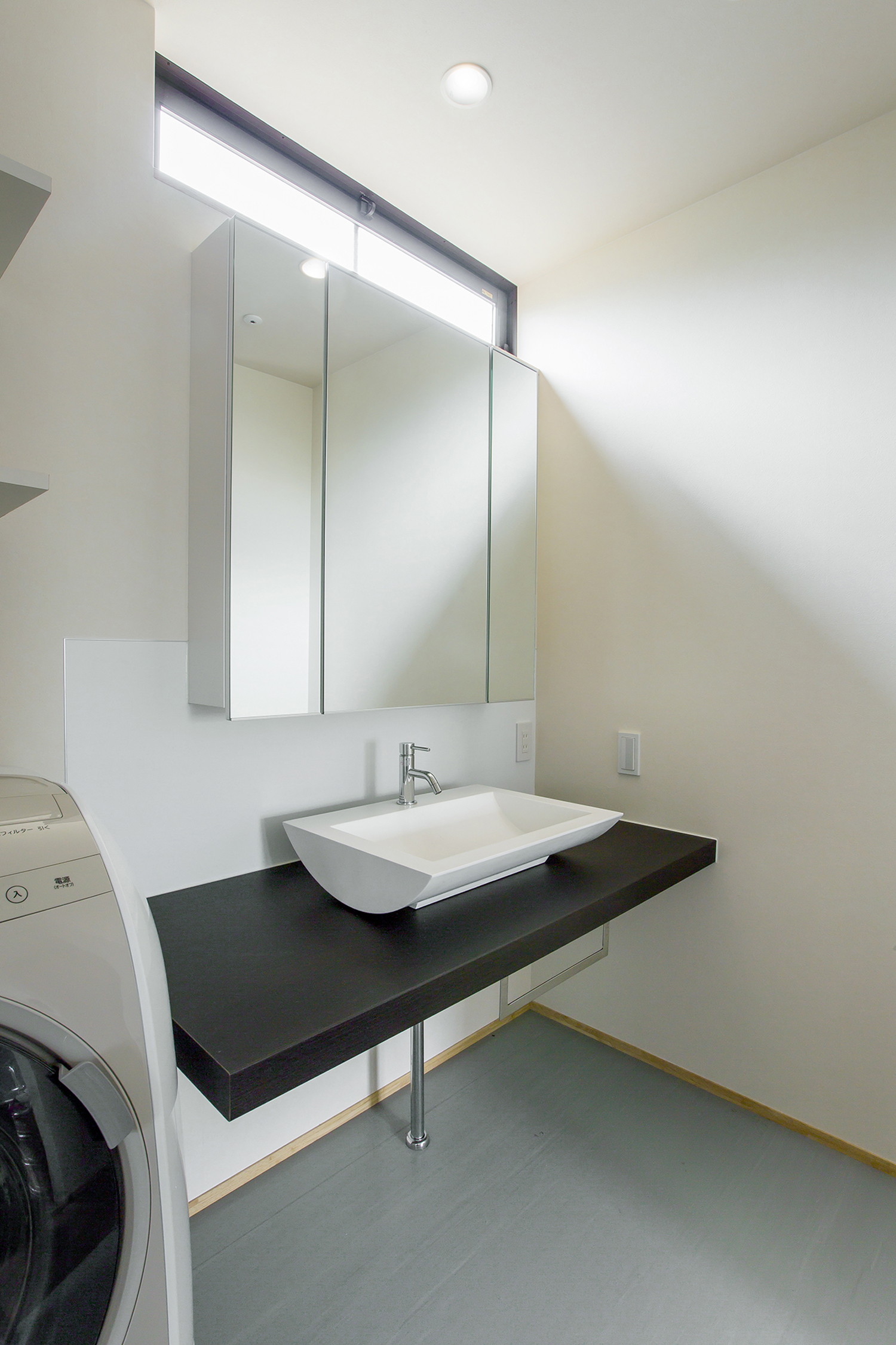 天井近くにスリット窓が取り付けられたシンプルなモノトーンの洗面所・デザイン住宅