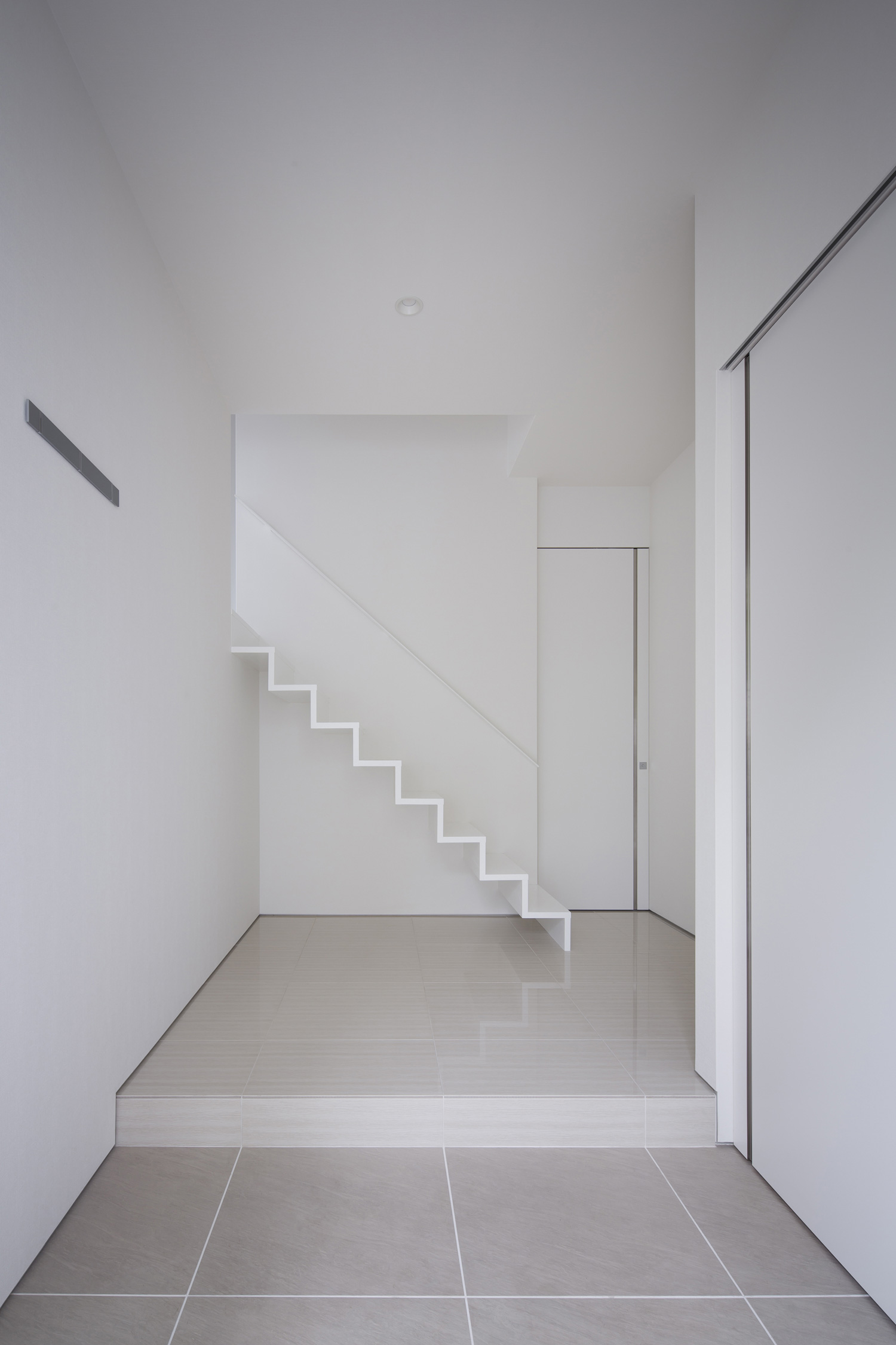正面に白い箱型階段があるシンプルな玄関・デザイン住宅
