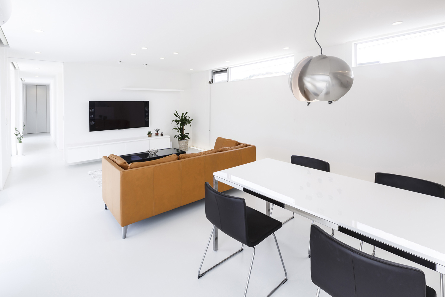 シンプルなモノトーンの空間にからし色のソファやおしゃれなペンダントライトのあるLDK・デザイン住宅