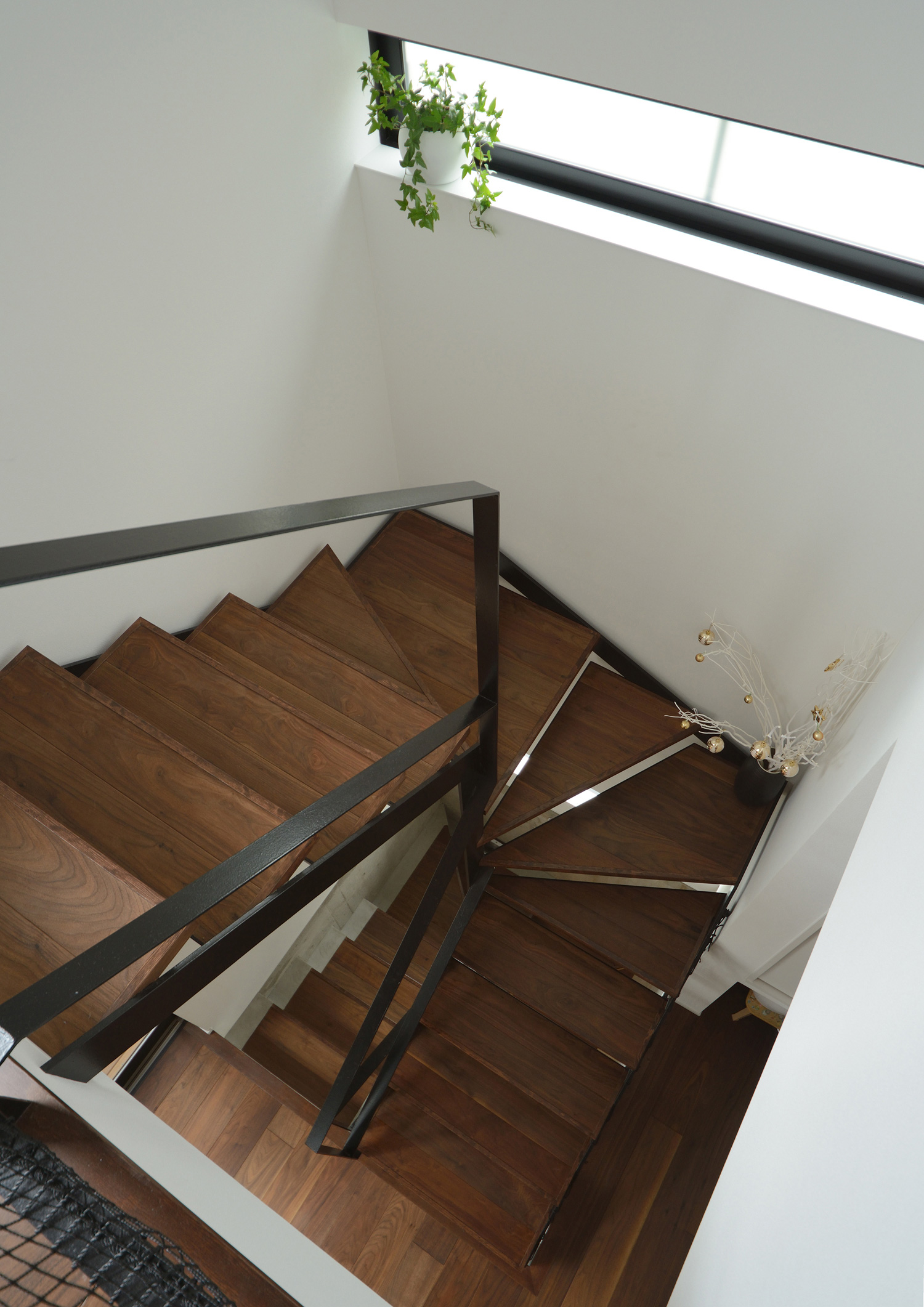 壁にスリット窓が取り付けられた黒いアイアンの手すり付きの木の螺旋階段・デザイン住宅