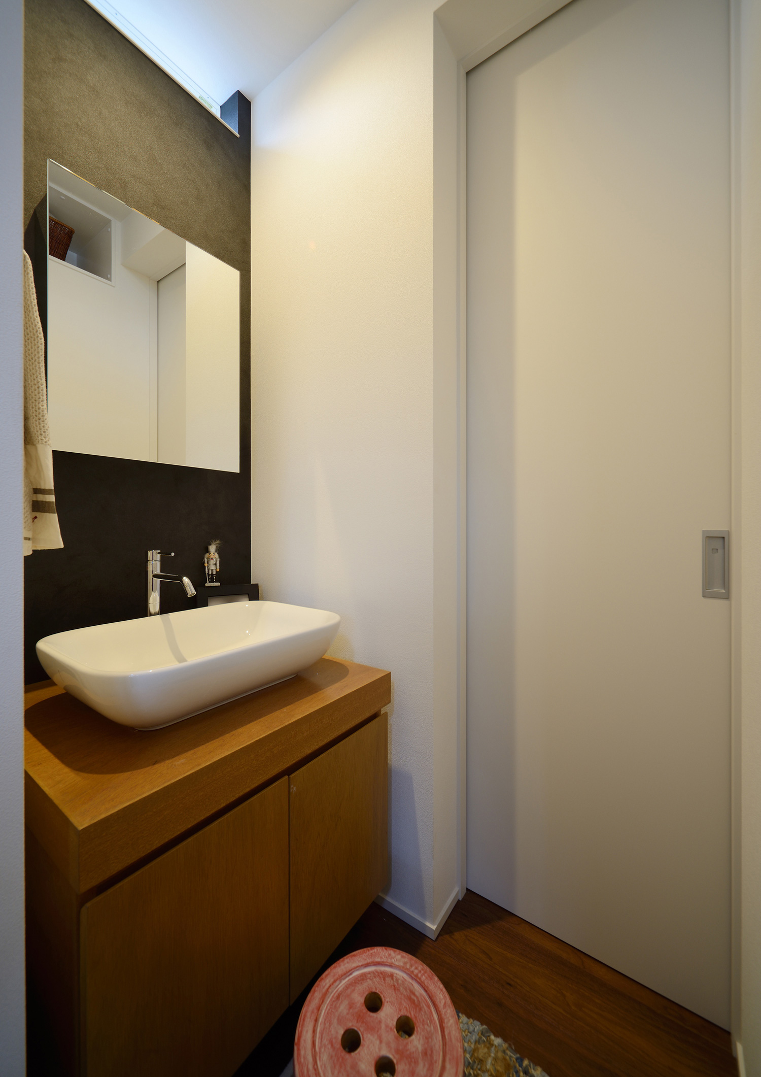 黒いアクセントクロスで木の収納があるコンパクトな手洗いカウンター・デザイン住宅