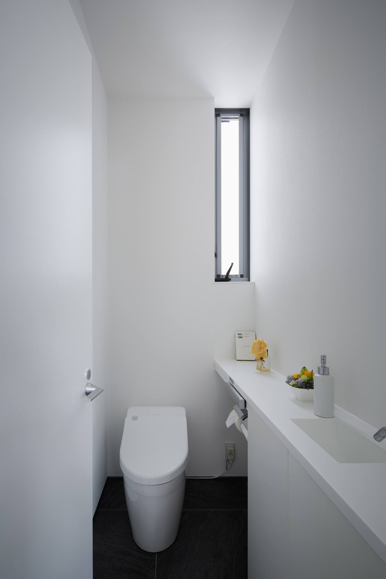 縦長のスリット窓や薄型手洗いがあるシンプルなトイレ・デザイン住宅