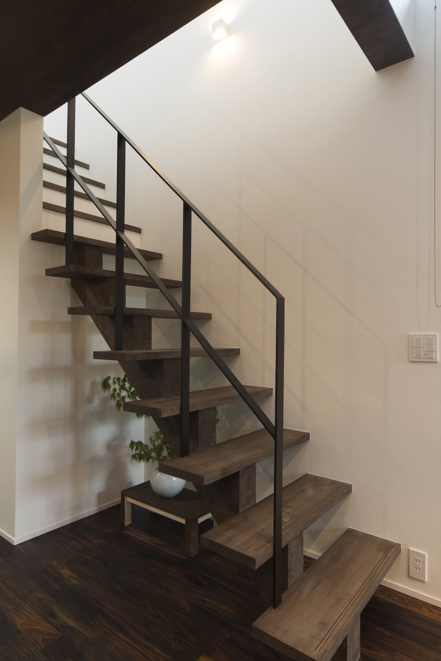 アイアンの手すりを取り付けた濃い色の木材のスケルトン階段・デザイン住宅