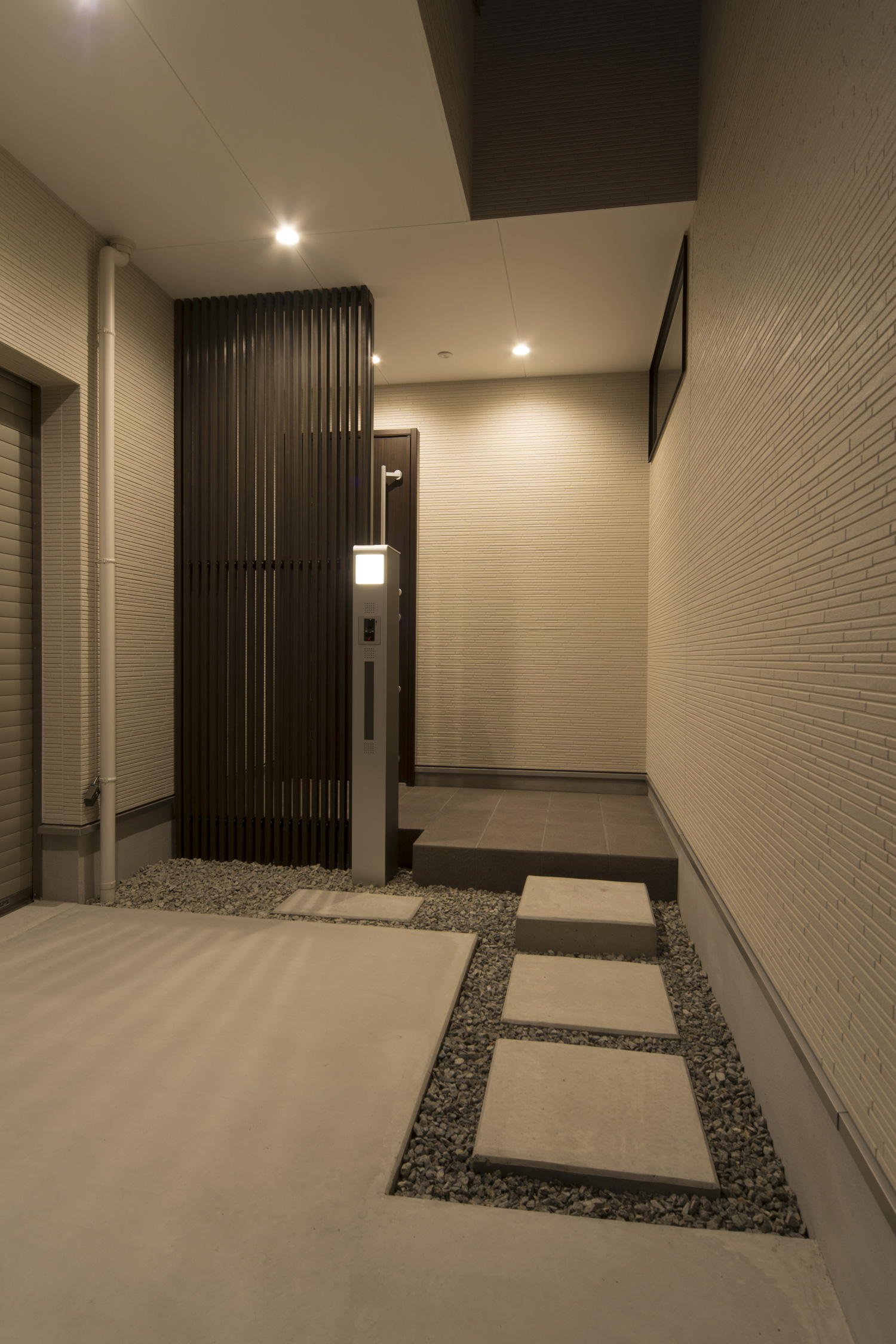 白い壁に黒いルーバーの目隠しを取り付けたモノトーンでプライベートな玄関・デザイン住宅