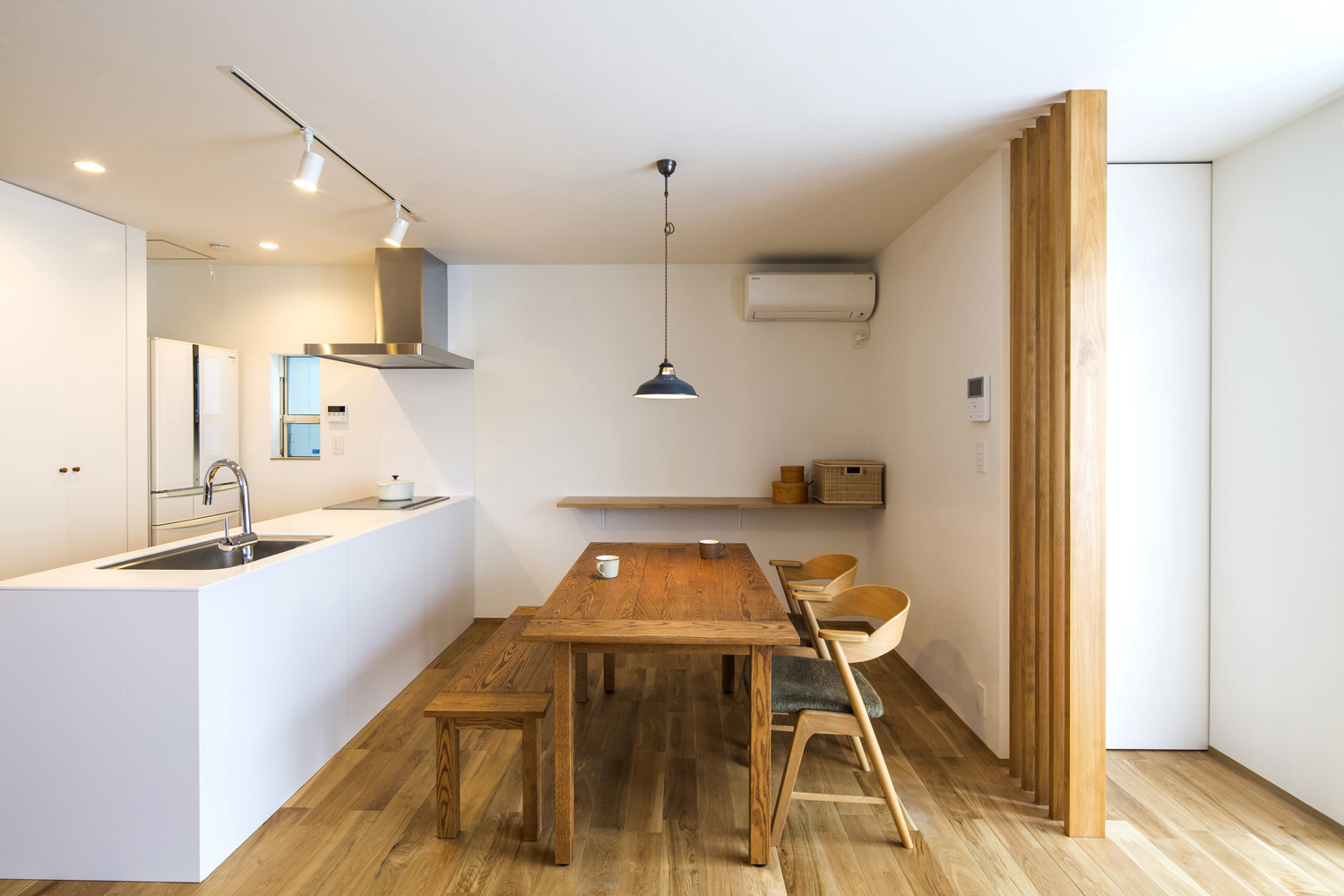 白いペニンシュラキッチンの向かいに無垢材のベンチとダイニングテーブルがあるLDK・デザイン住宅