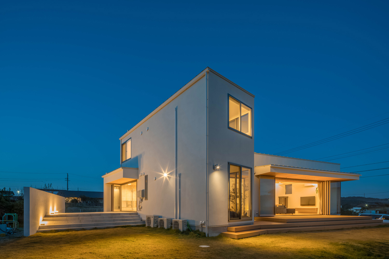 芝生の庭に囲まれた、白い外壁の家が照明に照らされる様子・デザイン住宅 注文住宅・デザイン住宅建築実例_『CASE495 舞台の家』_外観