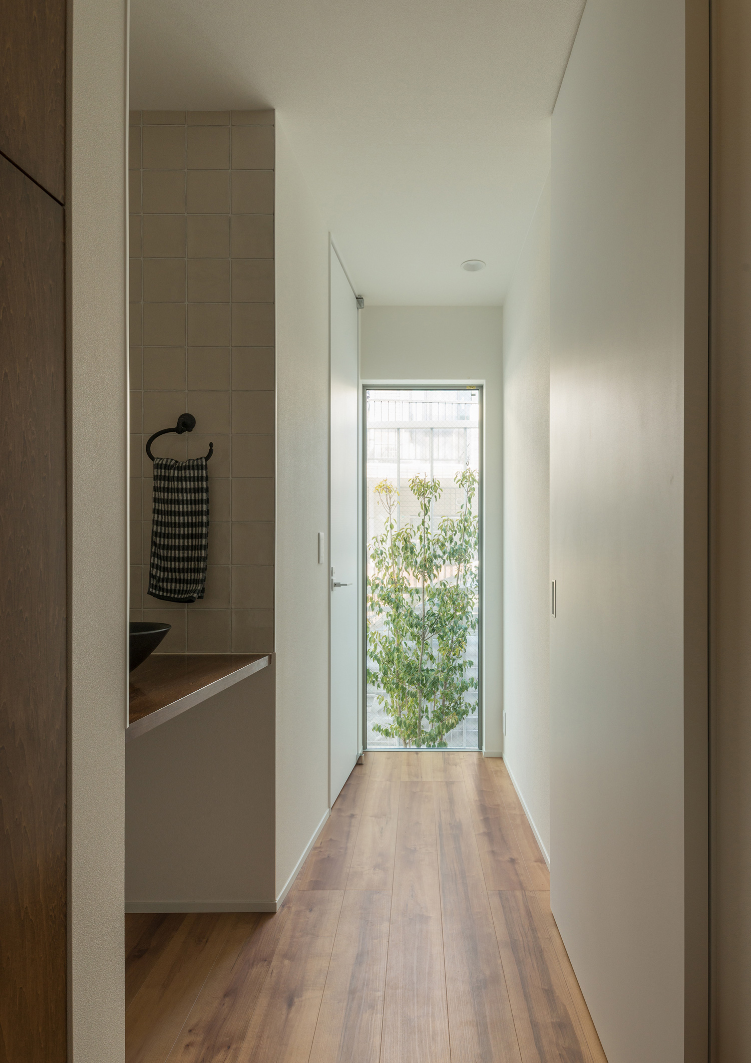 突き当りに植栽が見える窓があるフローリングの廊下・デザイン住宅 注文住宅・デザイン住宅建築実例_『CASE546 ウォールナットとガラスの家』_浴室・洗面所