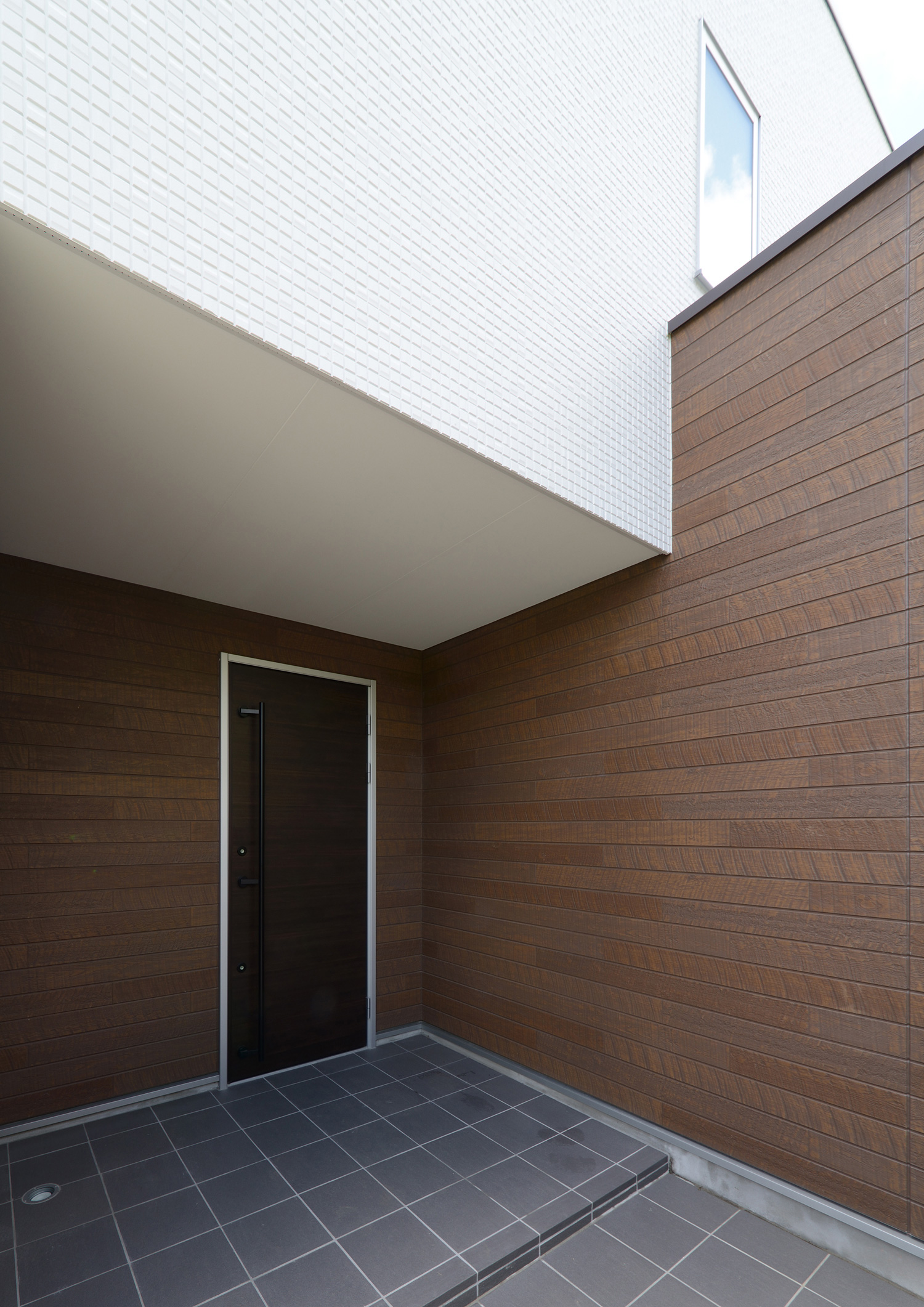 木目の壁に黒い玄関扉が取り付けられたタイルの玄関ポーチ・デザイン住宅 注文住宅・デザイン住宅建築実例_『CASE561 TOHFU-HOUSE』_外観