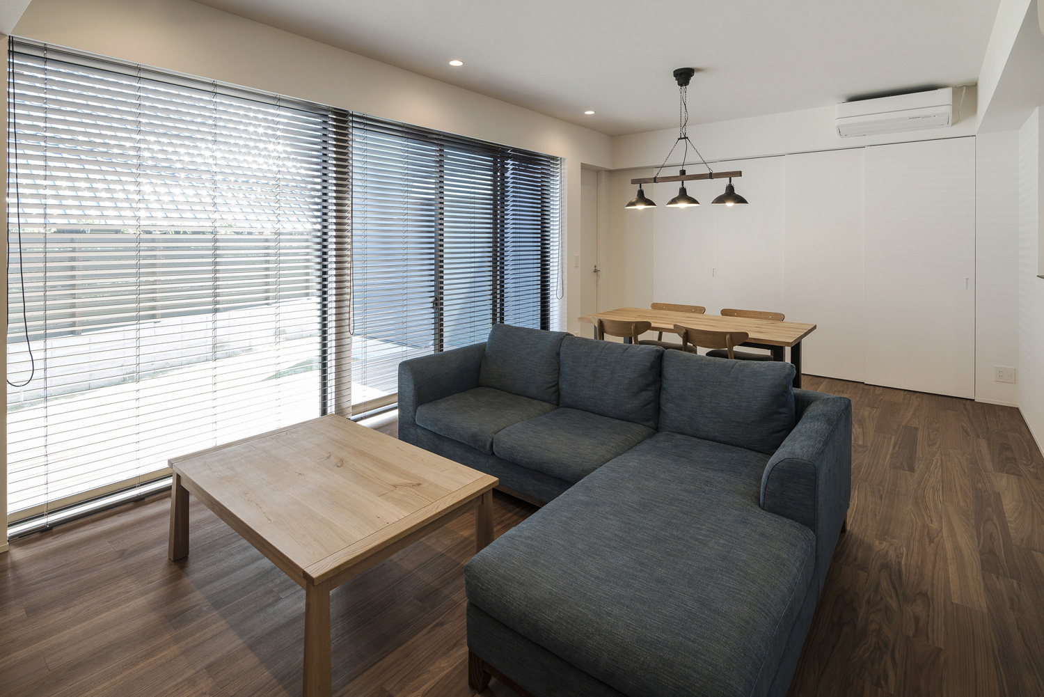 窓にブラインドを取り付けたL字ソファーを置いたフローリングのLDK・デザイン住宅 注文住宅・デザイン住宅建築実例_『CASE563 pocket』_LDK