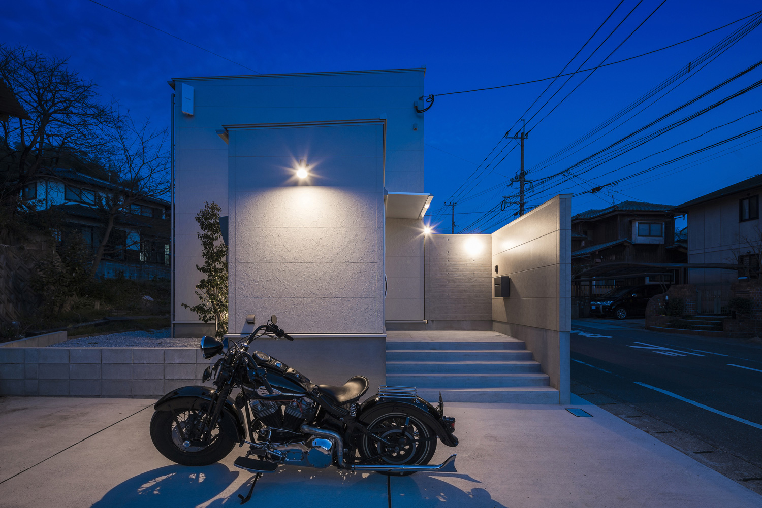 駐車スペースにあるバイクが外壁に取り付けられた照明に照らされる様子・デザイン住宅 注文住宅・デザイン住宅建築実例_『CASE567 lokki』_外観
