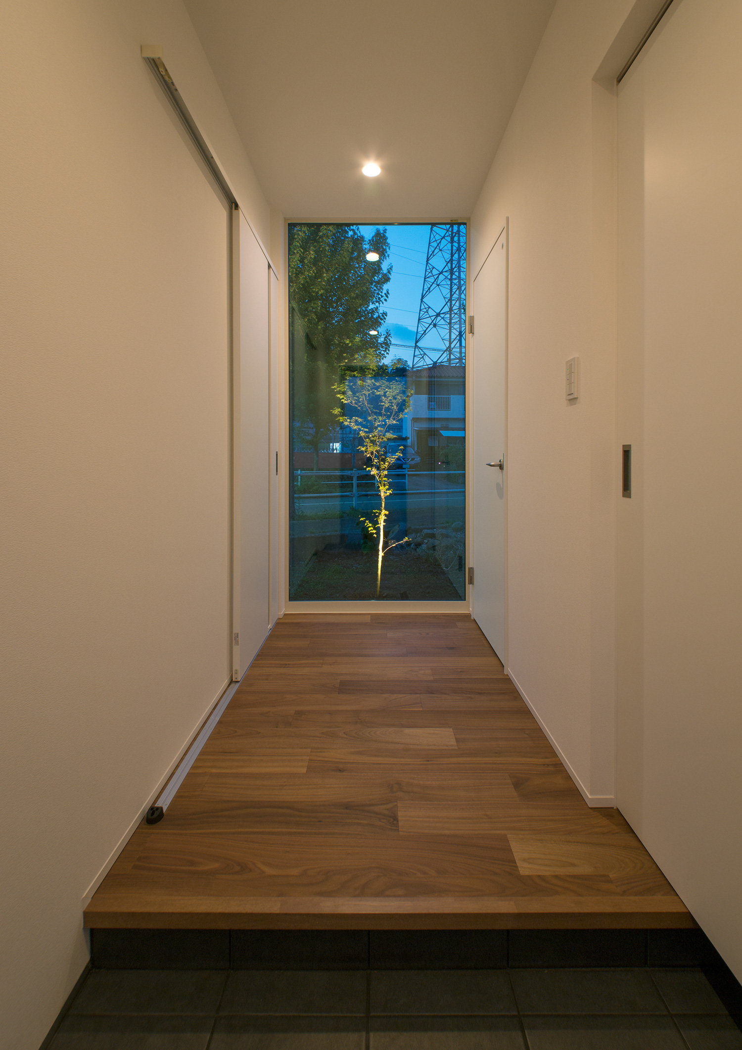 ライトアップされた植栽が見えるガラス窓がある廊下が、ダウンライトに照らされている様子・デザイン住宅 注文住宅・デザイン住宅建築実例_『CASE575 緑を楽しむ家』_玄関