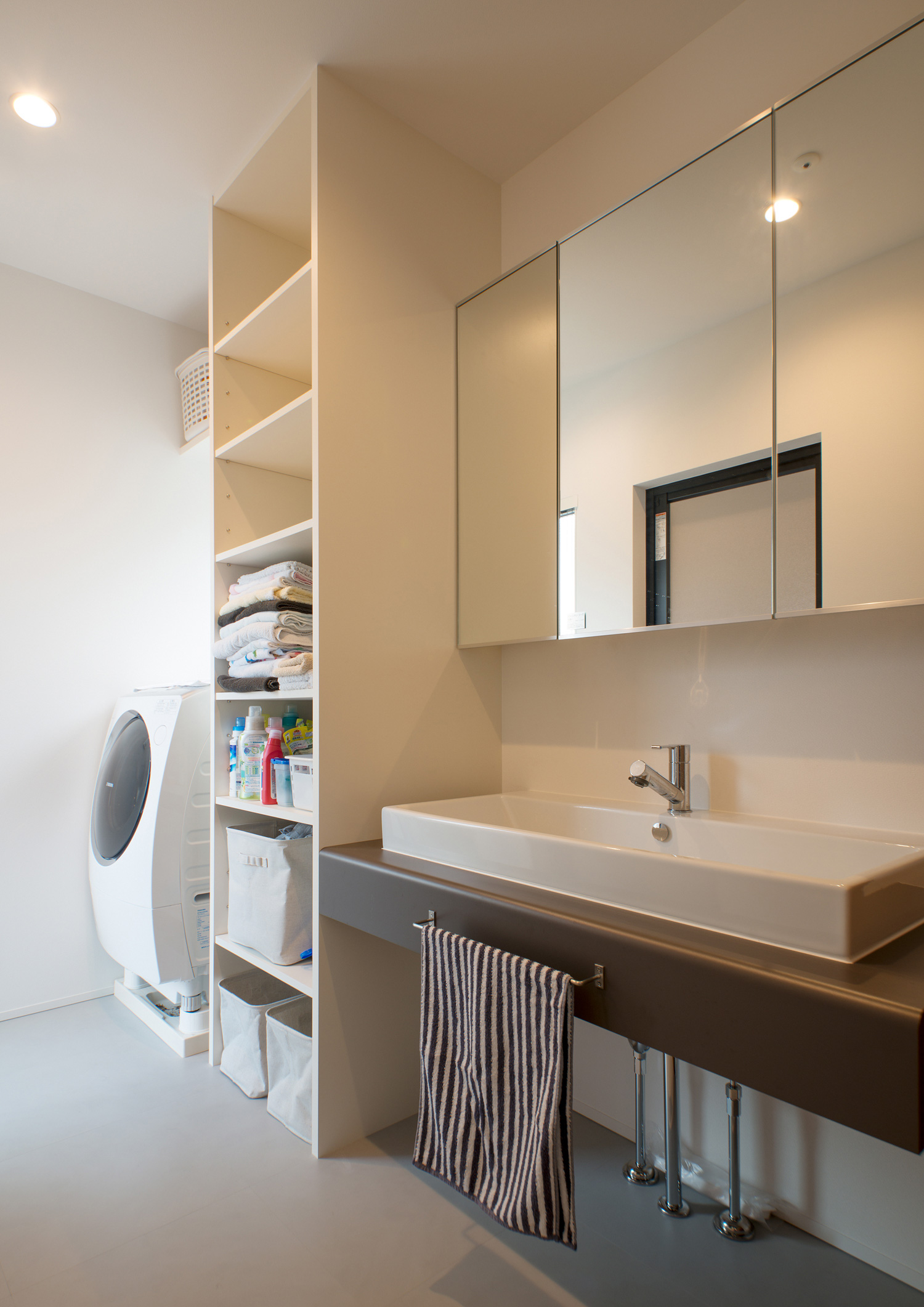 洗面台と洗濯機の間に収納棚を設けた白を基調とした洗面所・デザイン住宅 注文住宅・デザイン住宅建築実例_『CASE575 緑を楽しむ家』_浴室・洗面所